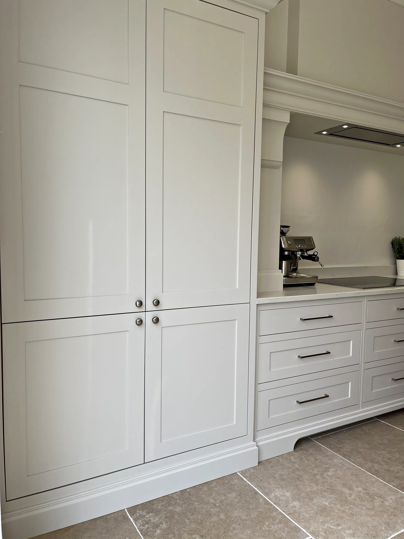 Tall pale painted cupboards with chrome knobs beside a run of drawers with bar handles