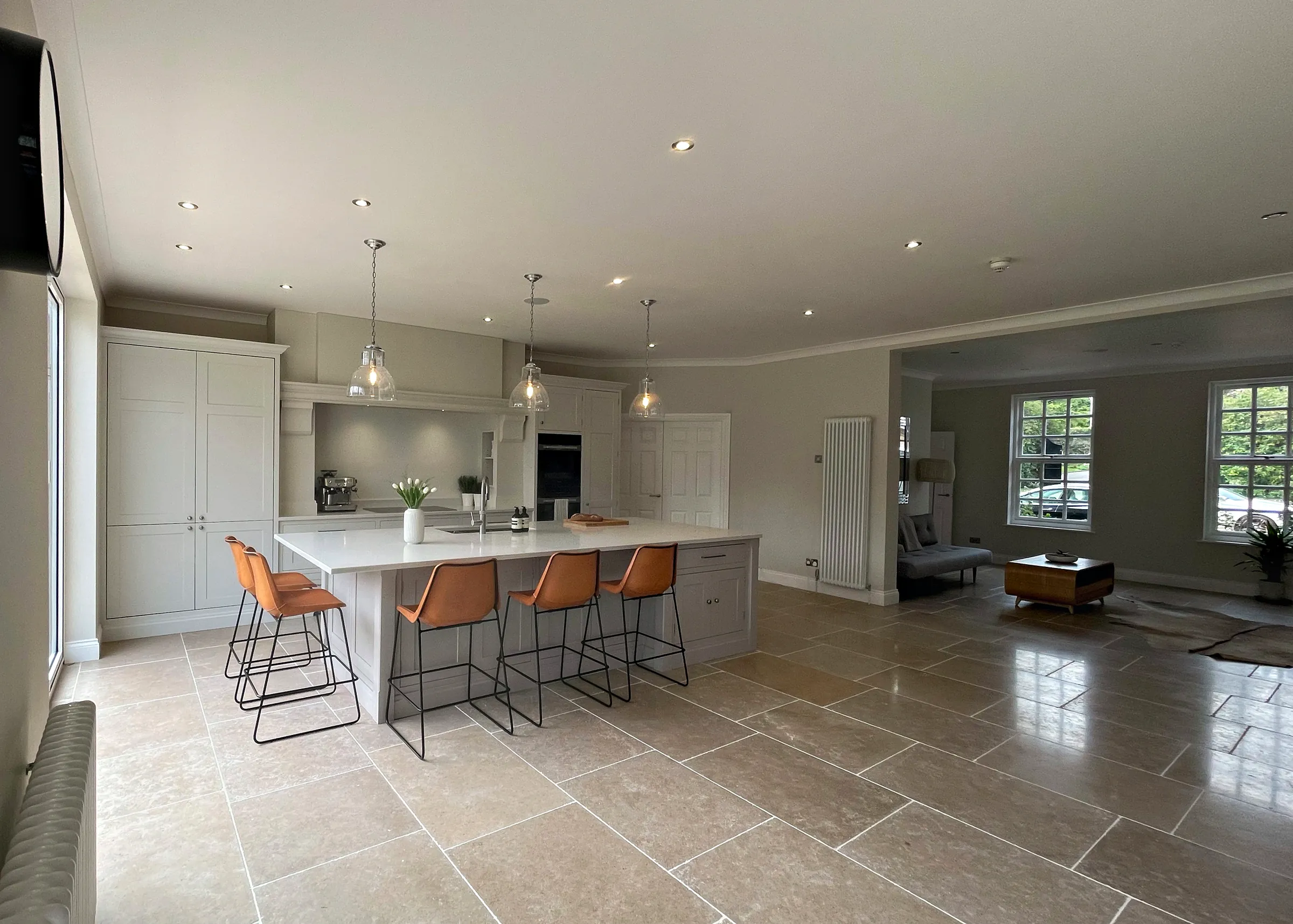 Open plan Birds Hill kitchen with a long pale grey island, leather bar stools and a limestone floor