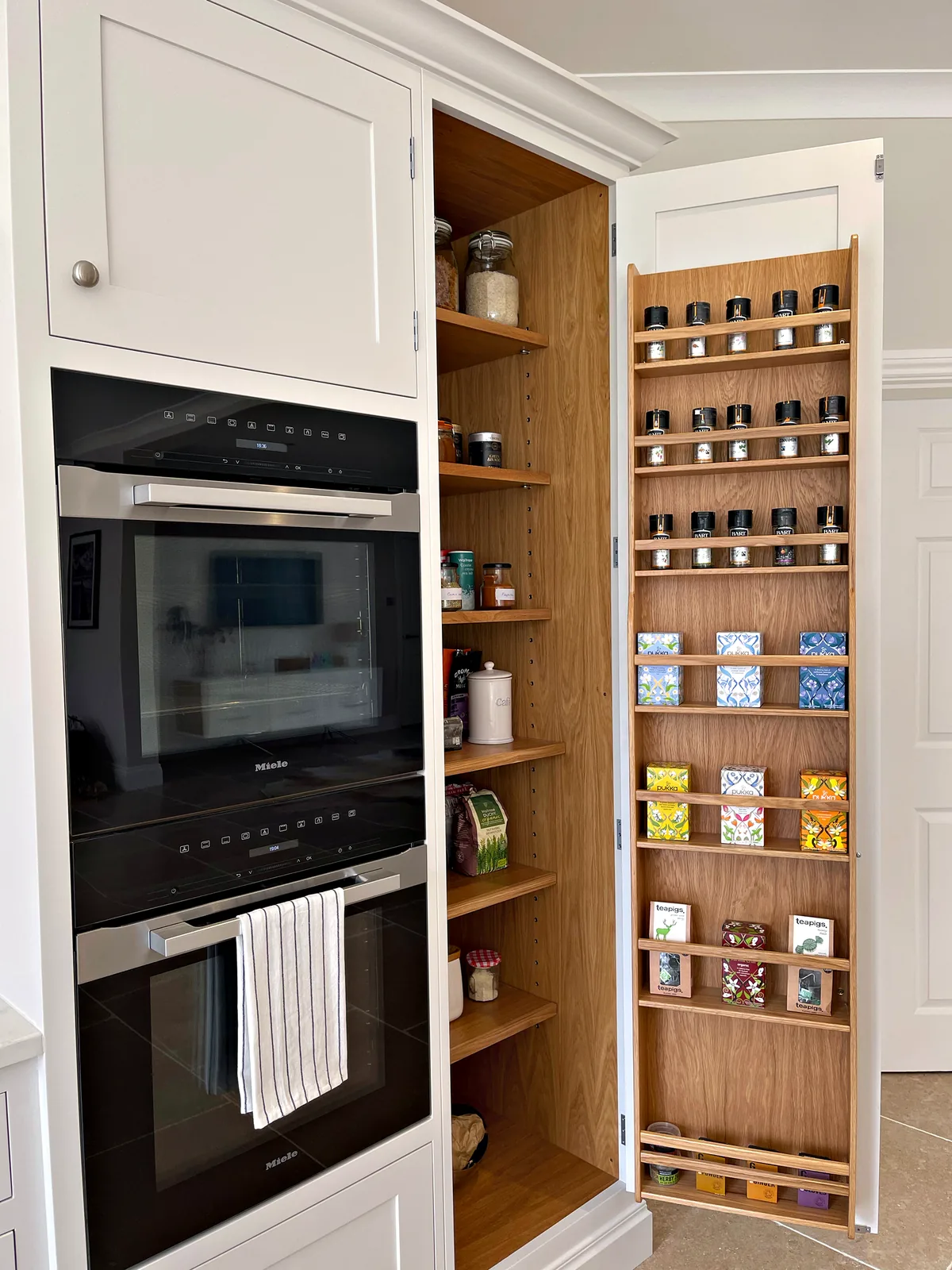 Bespoke larder with oak spice racks on the doors beside built in ovens