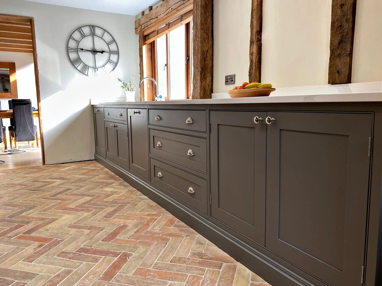 Long run of dark taupe in frame base cupboards and drawers with nickel knobs and cup handles on a herringbone brick floor at Barn Owls