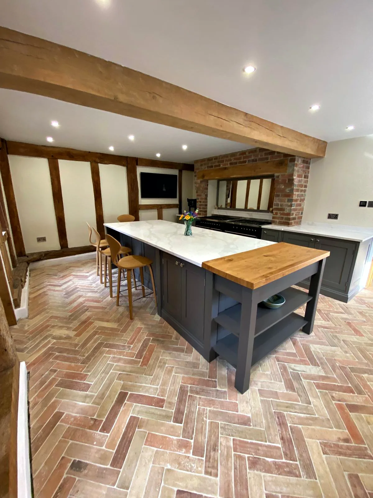 Timber framed barn kitchen with a dark taupe island, an oak breakfast bar end and a range cooker in a brick chimney breast