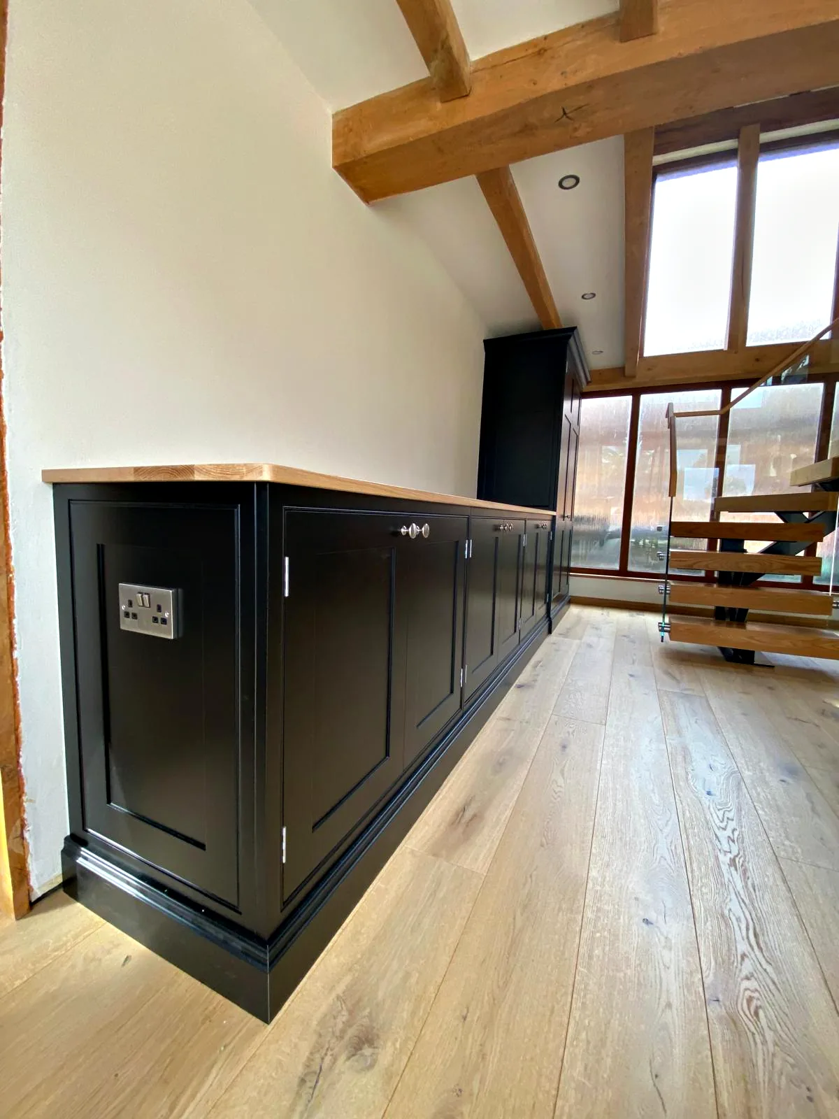 Long charcoal sideboard with an oak top in a double height barn room with a glazed gable and an open staircase