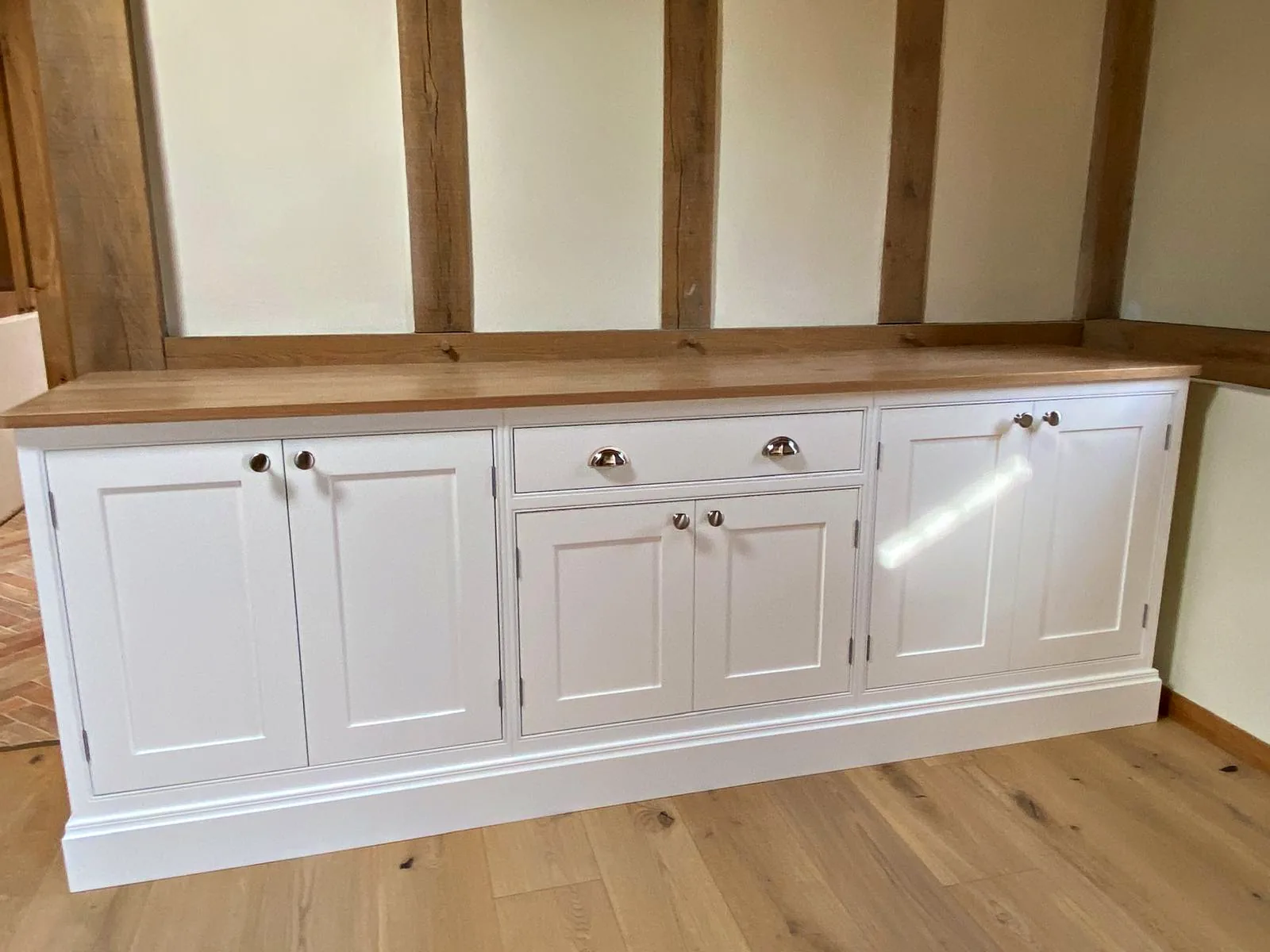 Off white sideboard with an oak top and nickel knobs against an oak framed wall