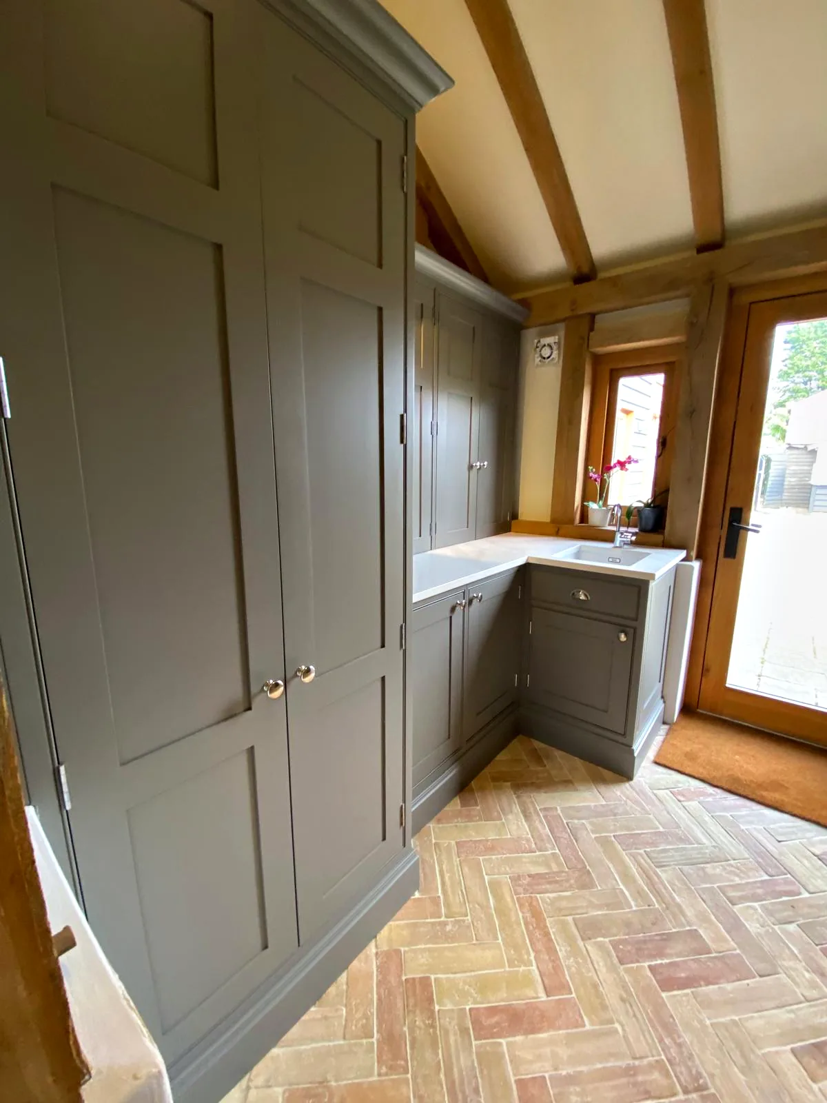 Tall dark taupe larder cupboards leading into a utility area with a sink beneath the oak frame