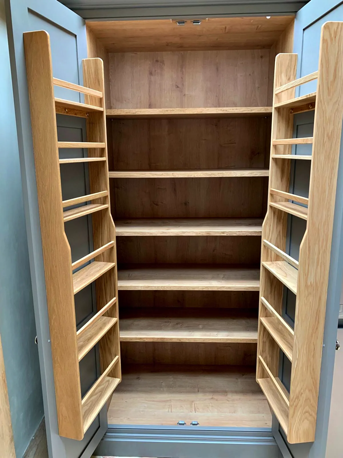 Tall larder open to show oak lined shelves and full height oak door racks