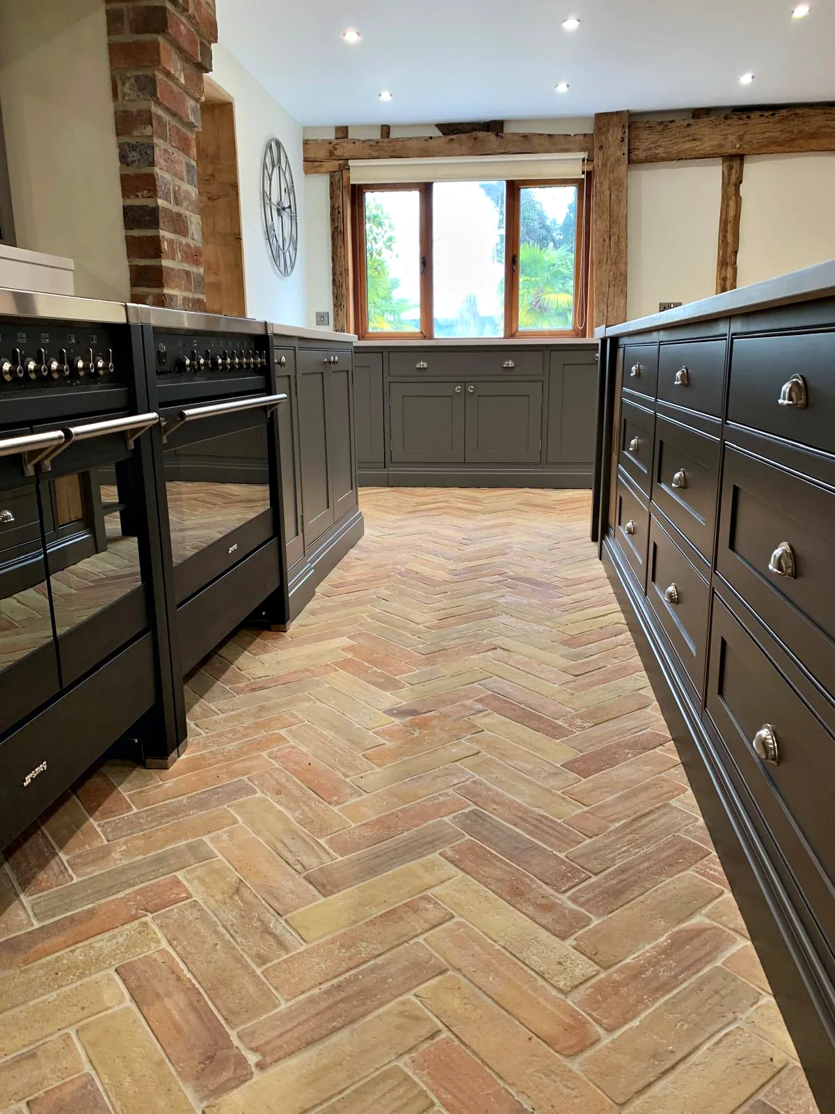 Herringbone brick floor running between twin range cookers and the island drawers towards the window