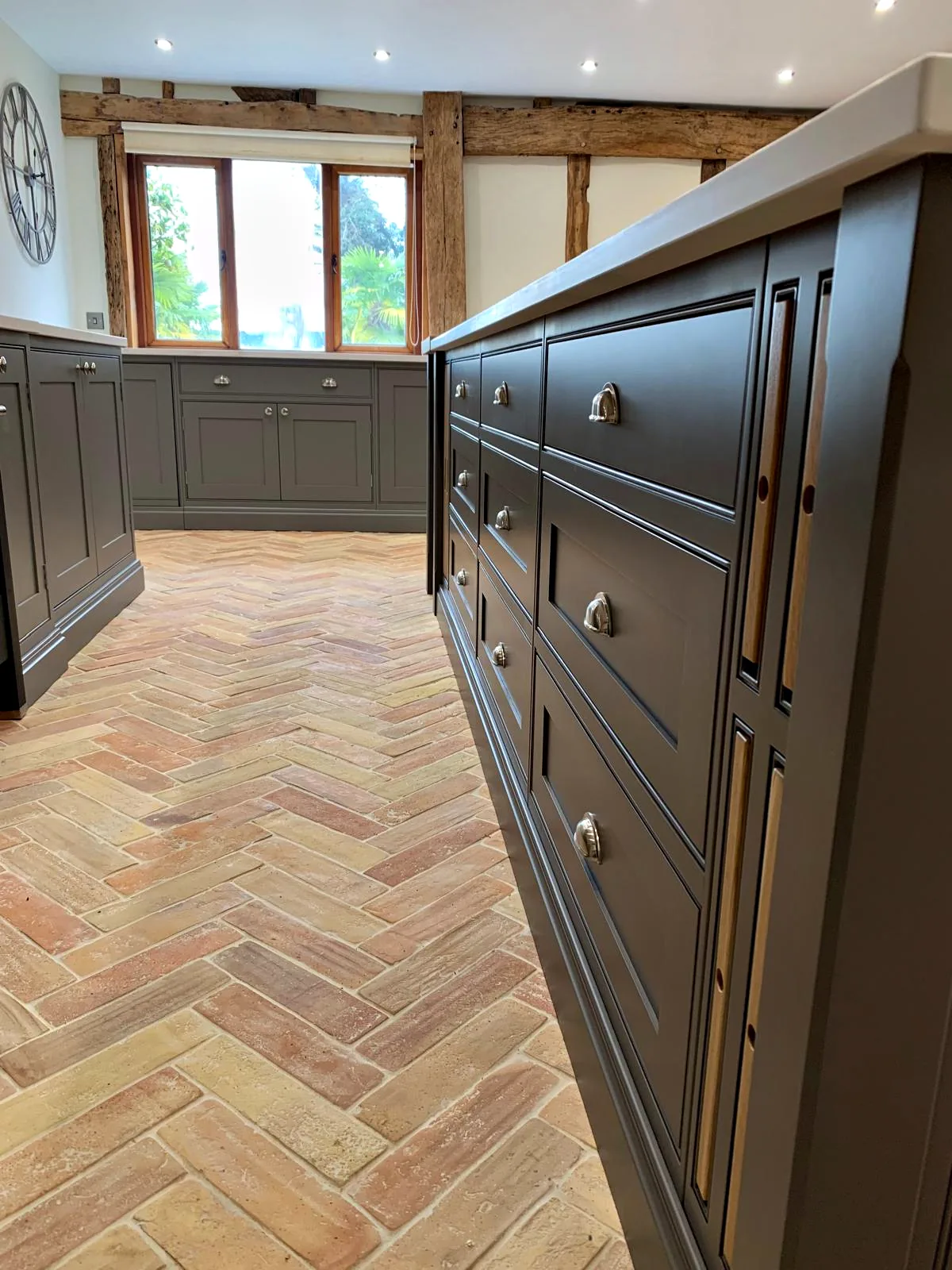 Long dark taupe island with deep drawers and nickel cup handles on a herringbone brick floor