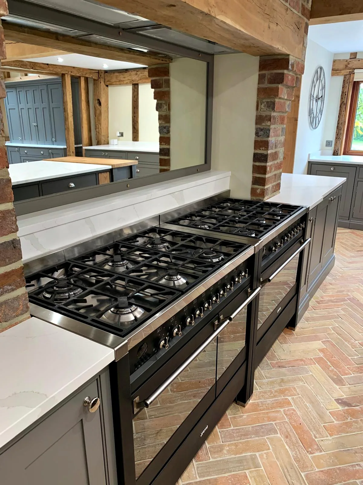 Twin black range cookers below a mirrored splashback between brick piers