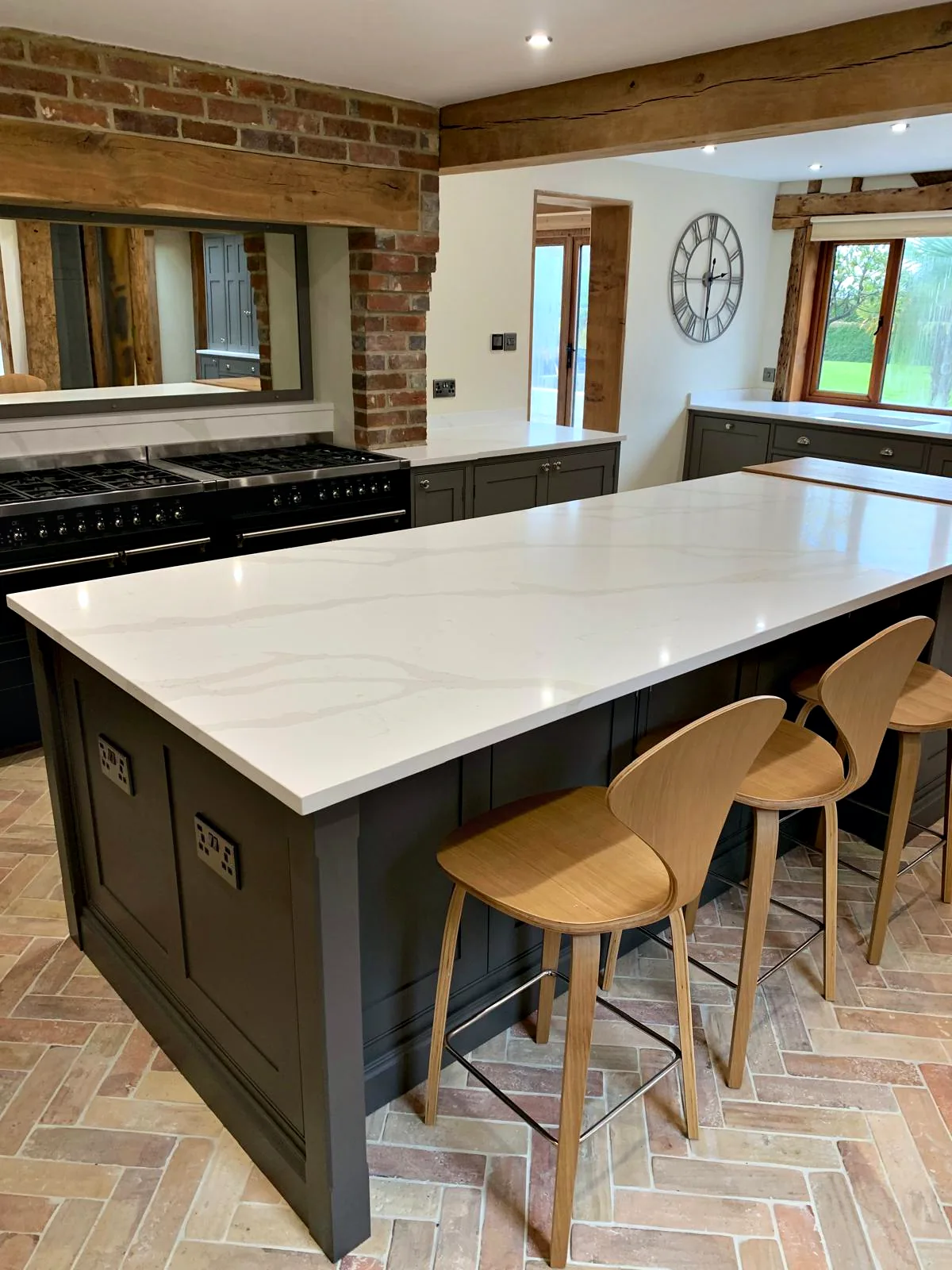 Dark taupe island with a white veined quartz top and oak bar stools in front of the range wall