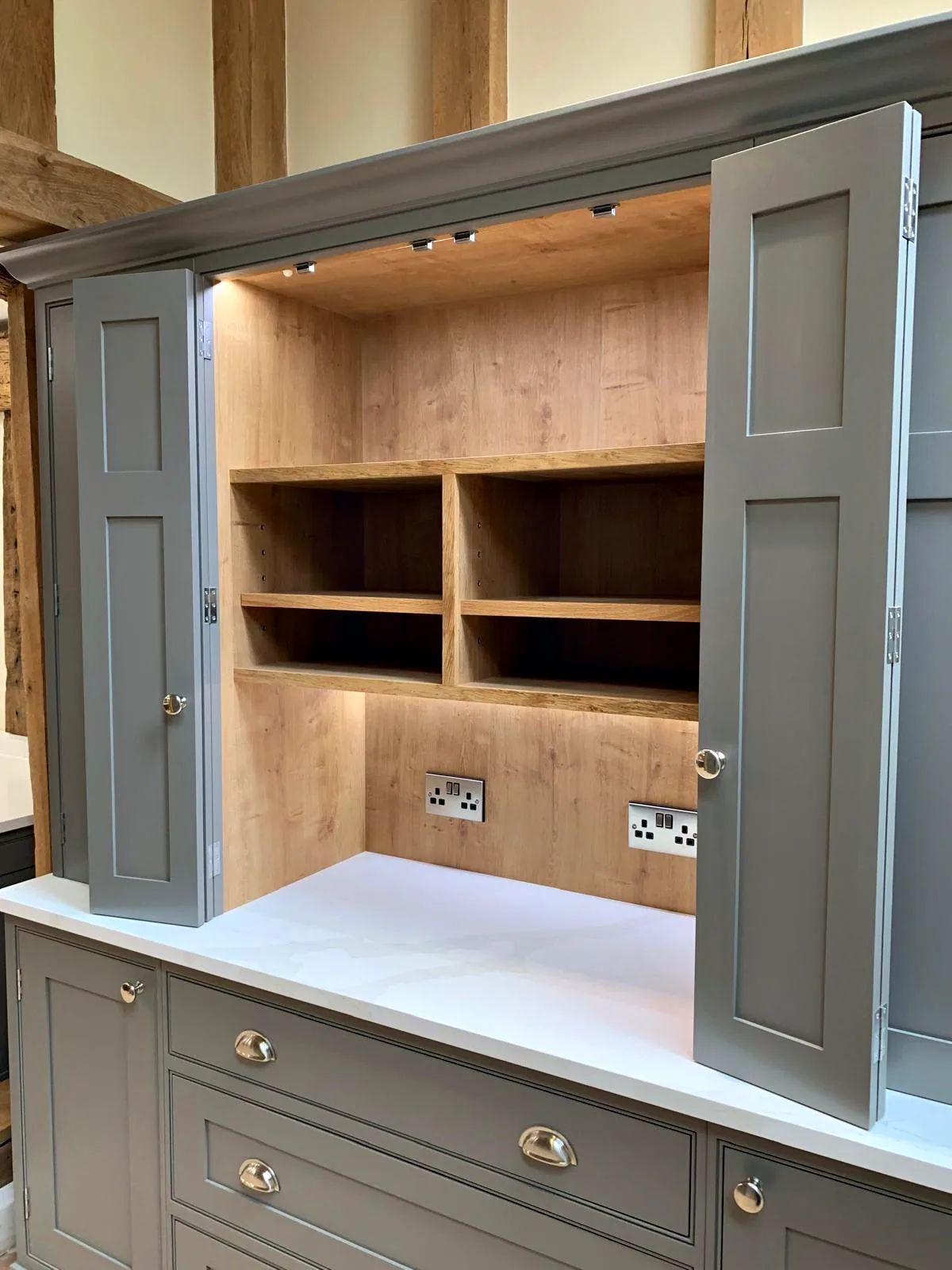 Dark taupe dresser larder with bifold doors open on an oak lined niche over drawers with cup handles