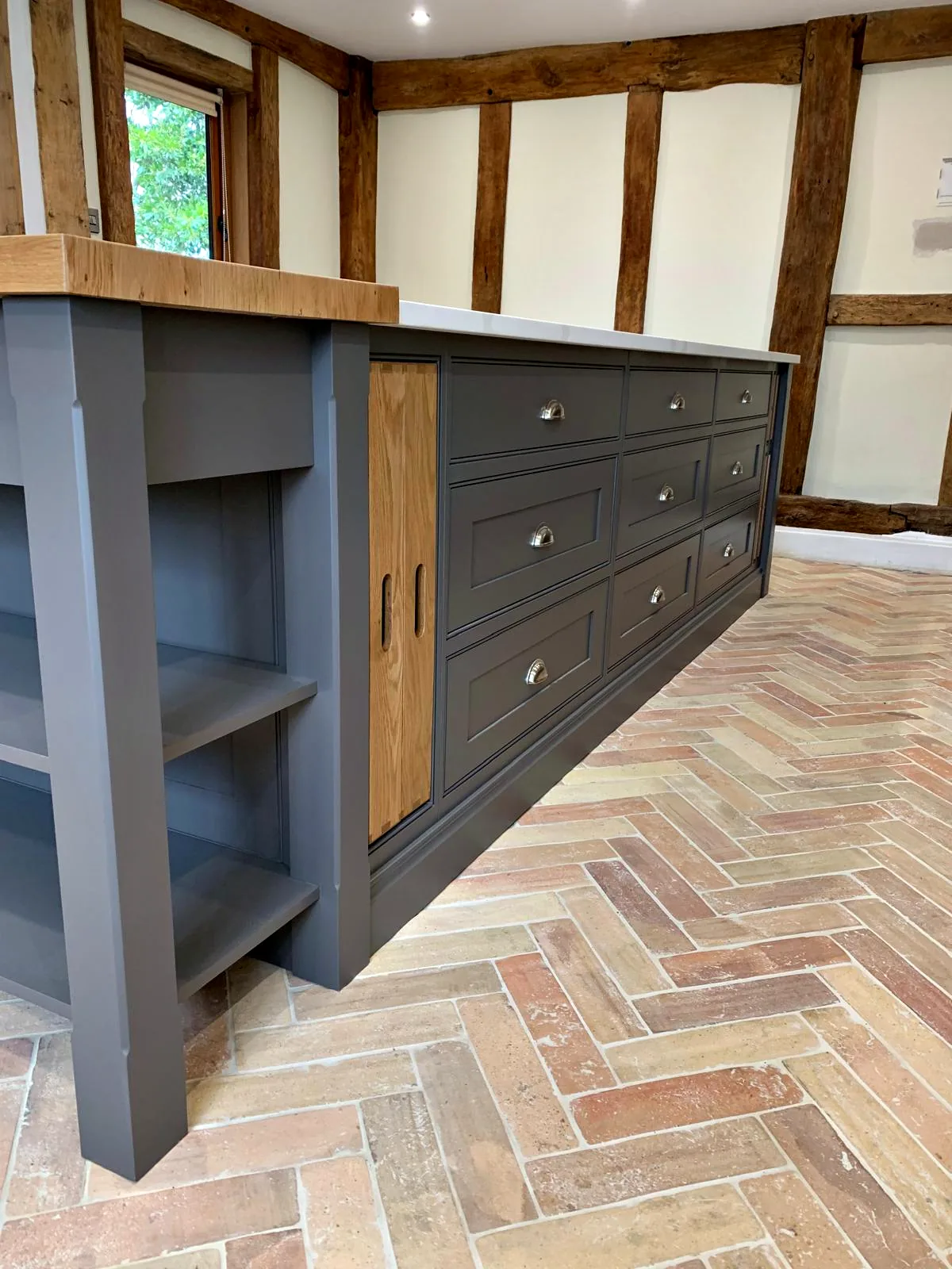 End of a dark taupe island with open shelves and an oak breakfast bar top under oak beams