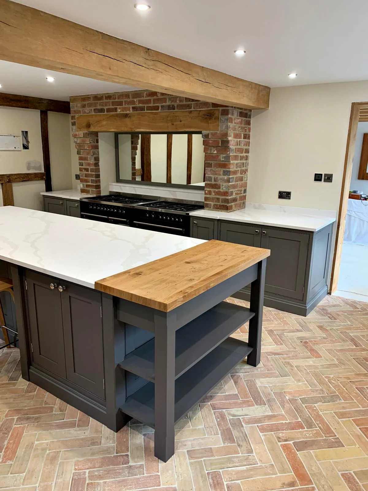 Island with an oak topped end and open shelves in front of the range set into a brick chimney breast