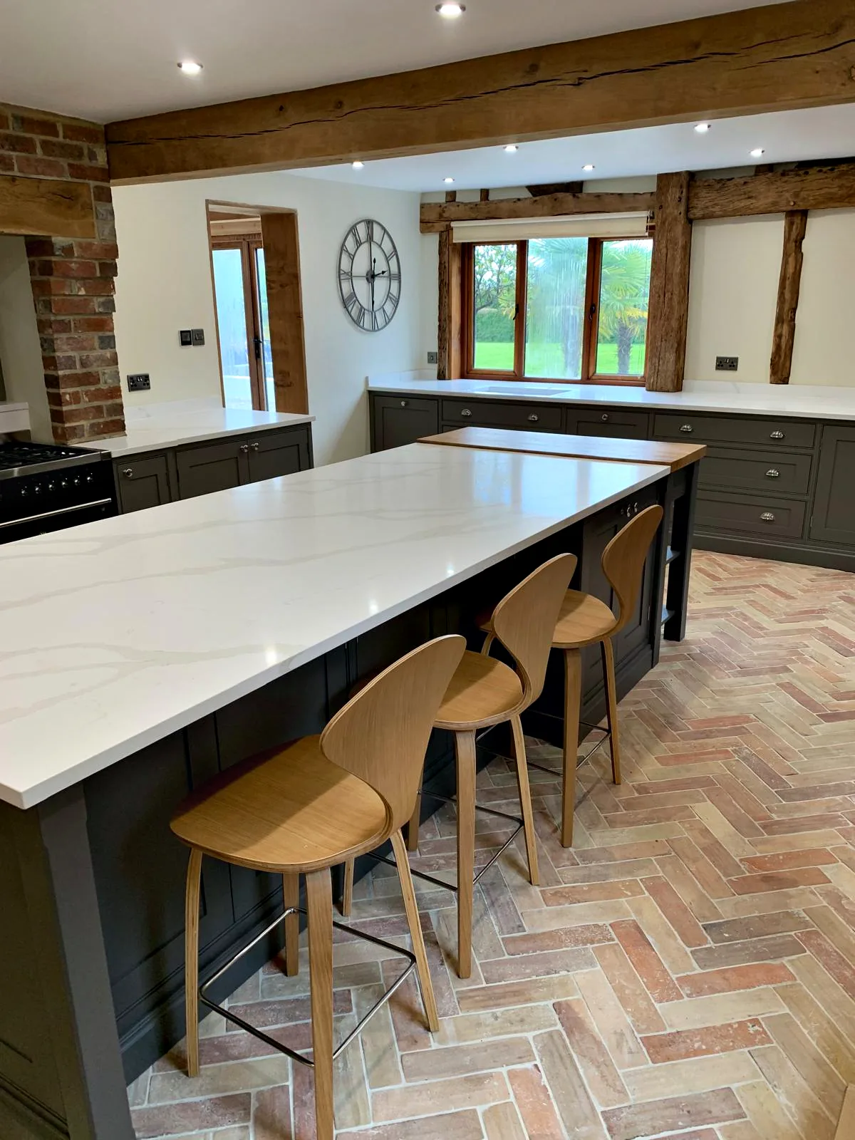 Long island with a white quartz top and oak bar stools in an oak beamed kitchen