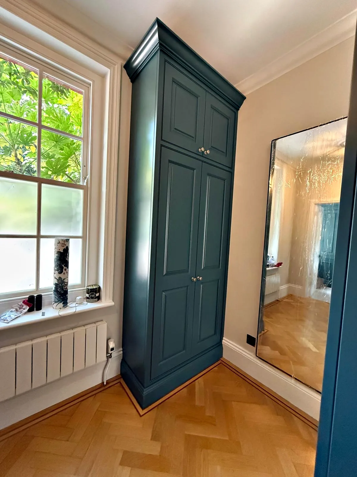 Tall deep teal cupboard beside a sash window in the hallway