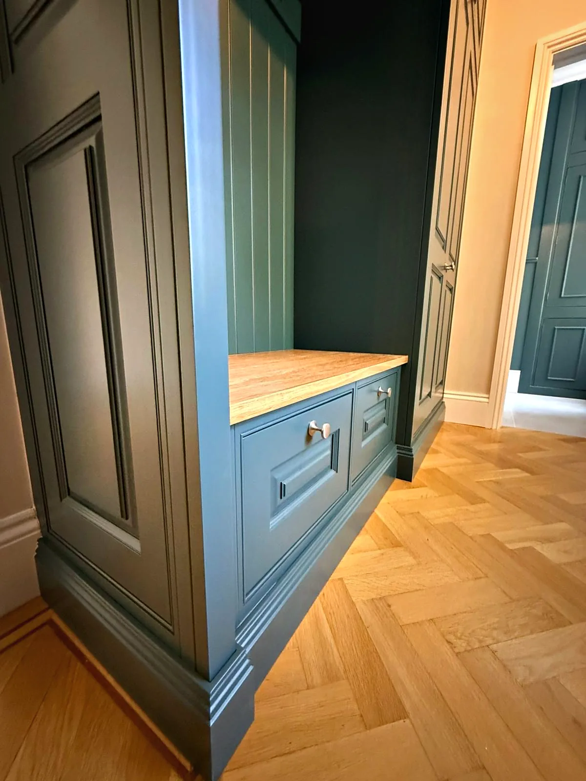 End of the teal hall unit with a raised and fielded side panel and oak topped drawers on herringbone parquet