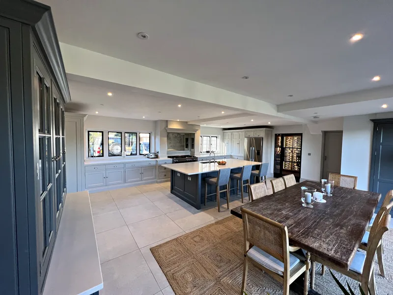Open plan kitchen and dining area seen past a tall slate grey glazed dresser, with a slate blue island beyond