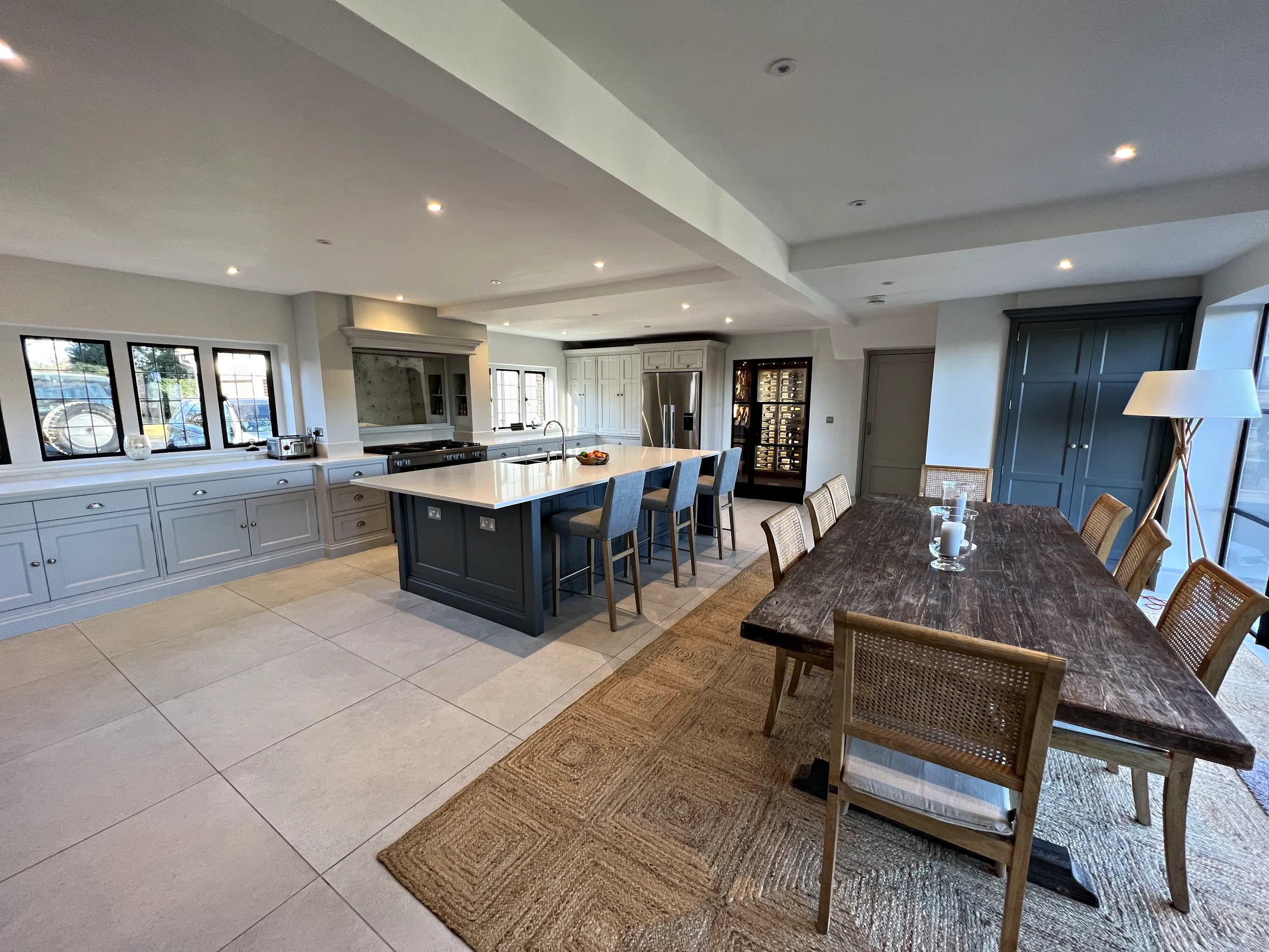 Rustic dining table before a slate blue island, a pale grey wall run and black steel glazed doors