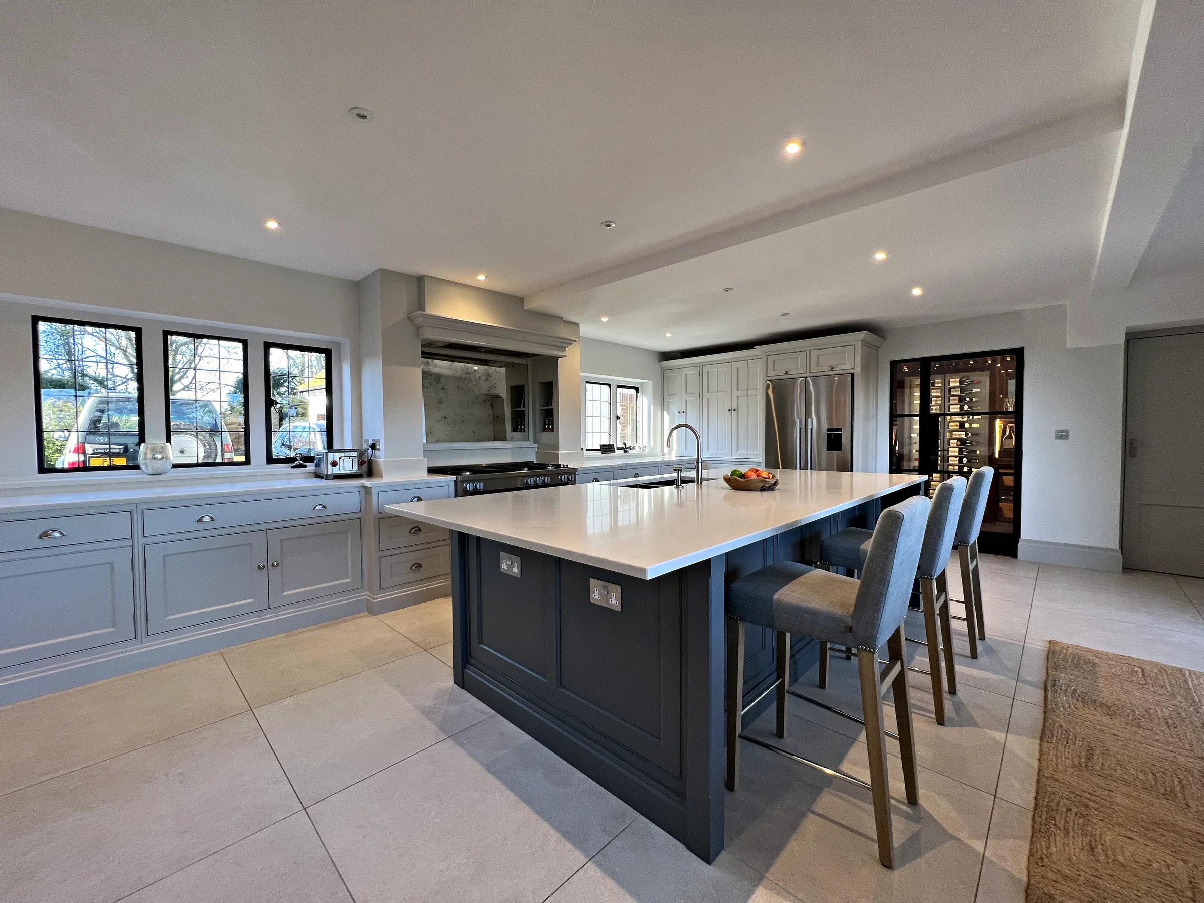 Slate blue island with four bar stools, a pale grey wall run under leaded windows and a range