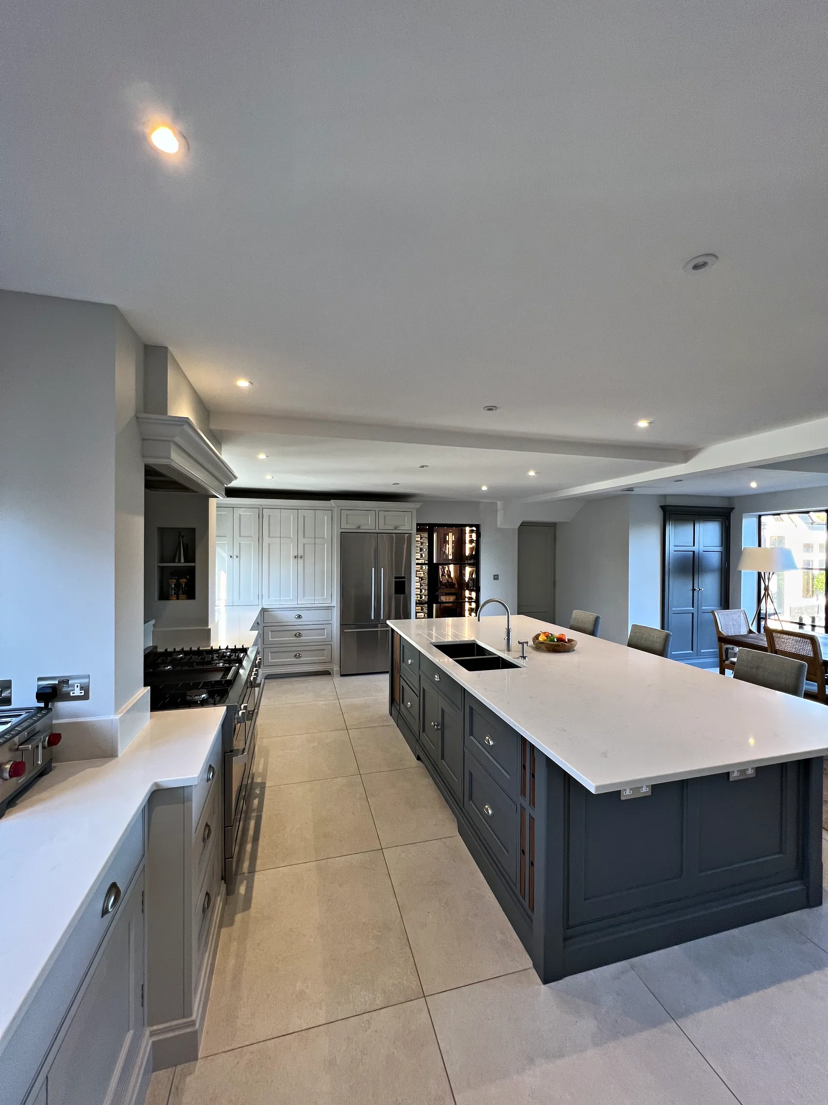 Slate blue island with twin sinks beside a pale grey range run, glazed doors at the far end