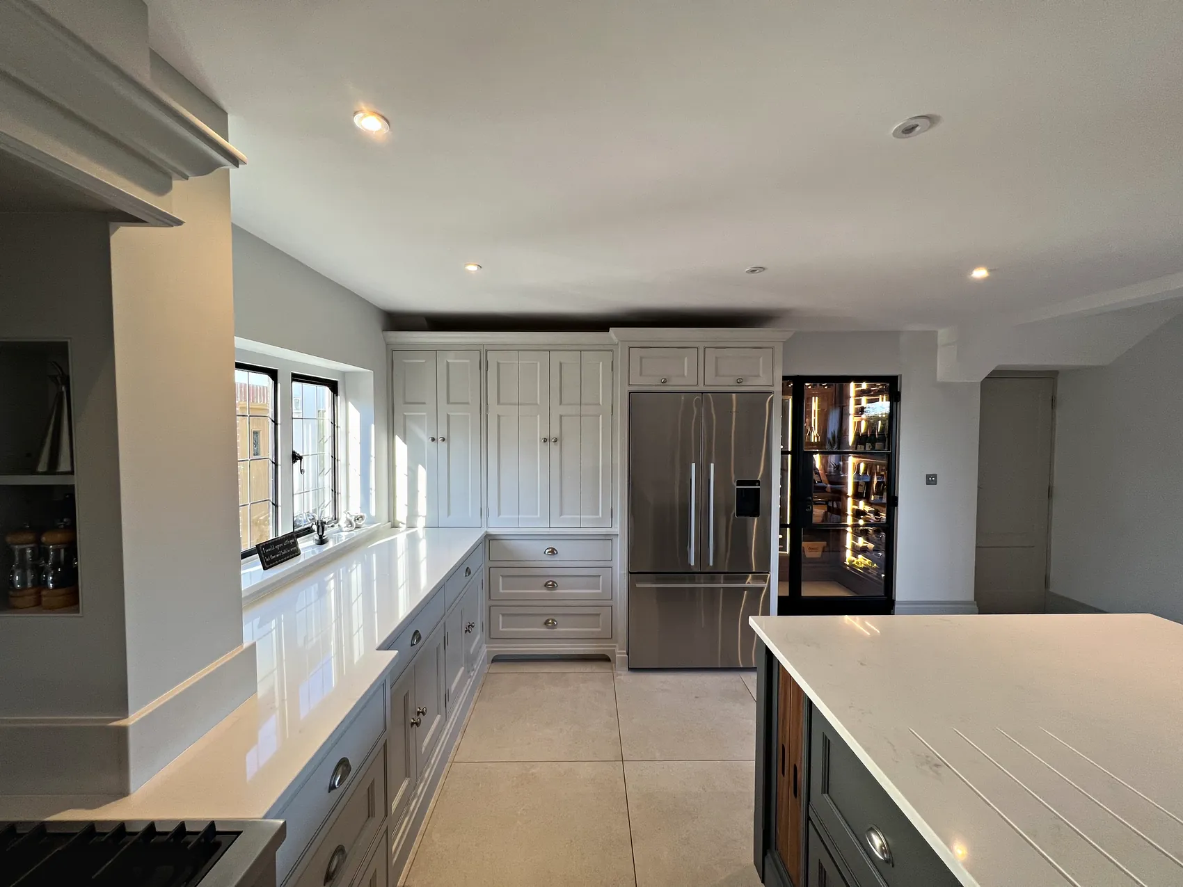 Tall pale grey units around the fridge freezer with the island corner in front