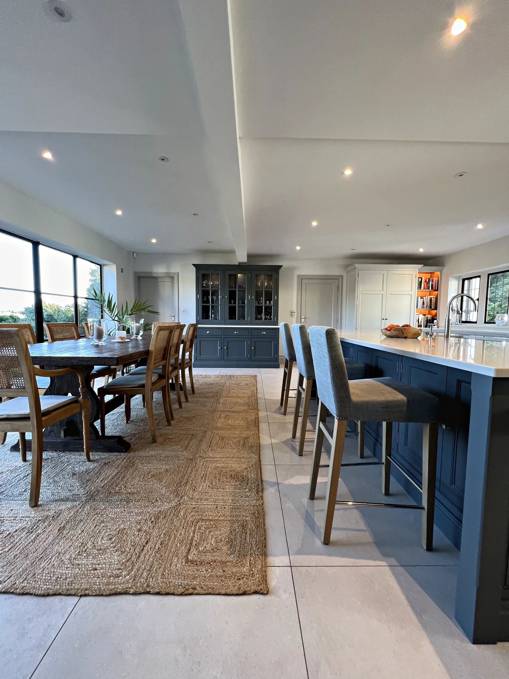 Kitchen diner with a dining table, slate blue island stools and a glazed dresser at the far end