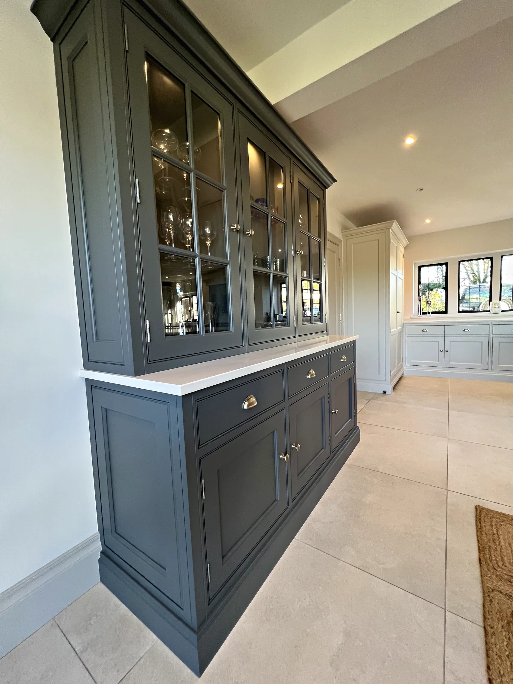 Slate grey glazed dresser with cup handled drawers, seen from the side with the pale kitchen run beyond