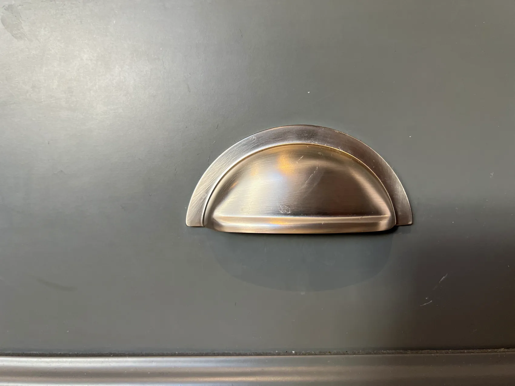 Brushed nickel cup handle on a slate grey drawer front
