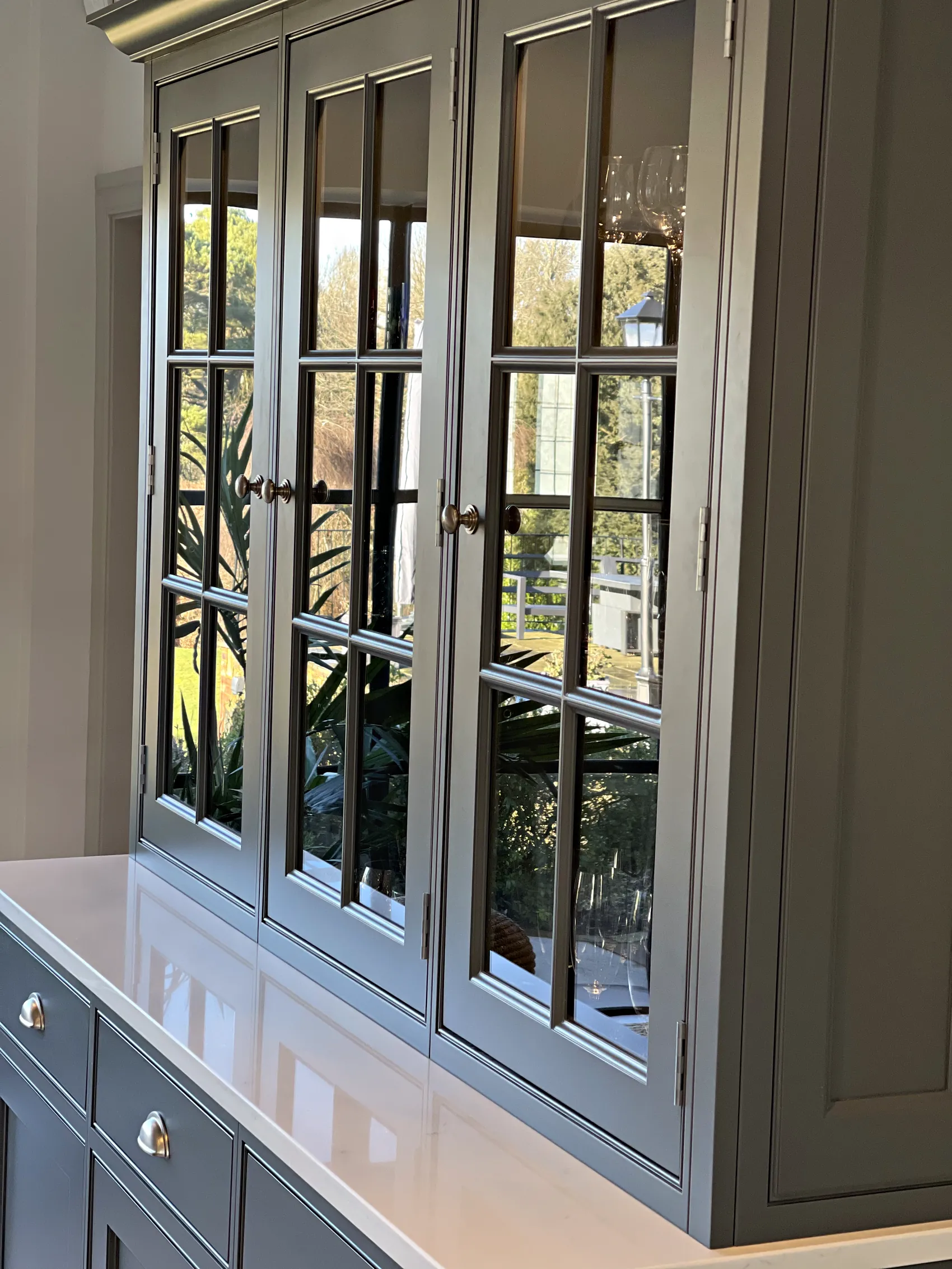 Slate grey glazed dresser doors with the garden reflected in the glass