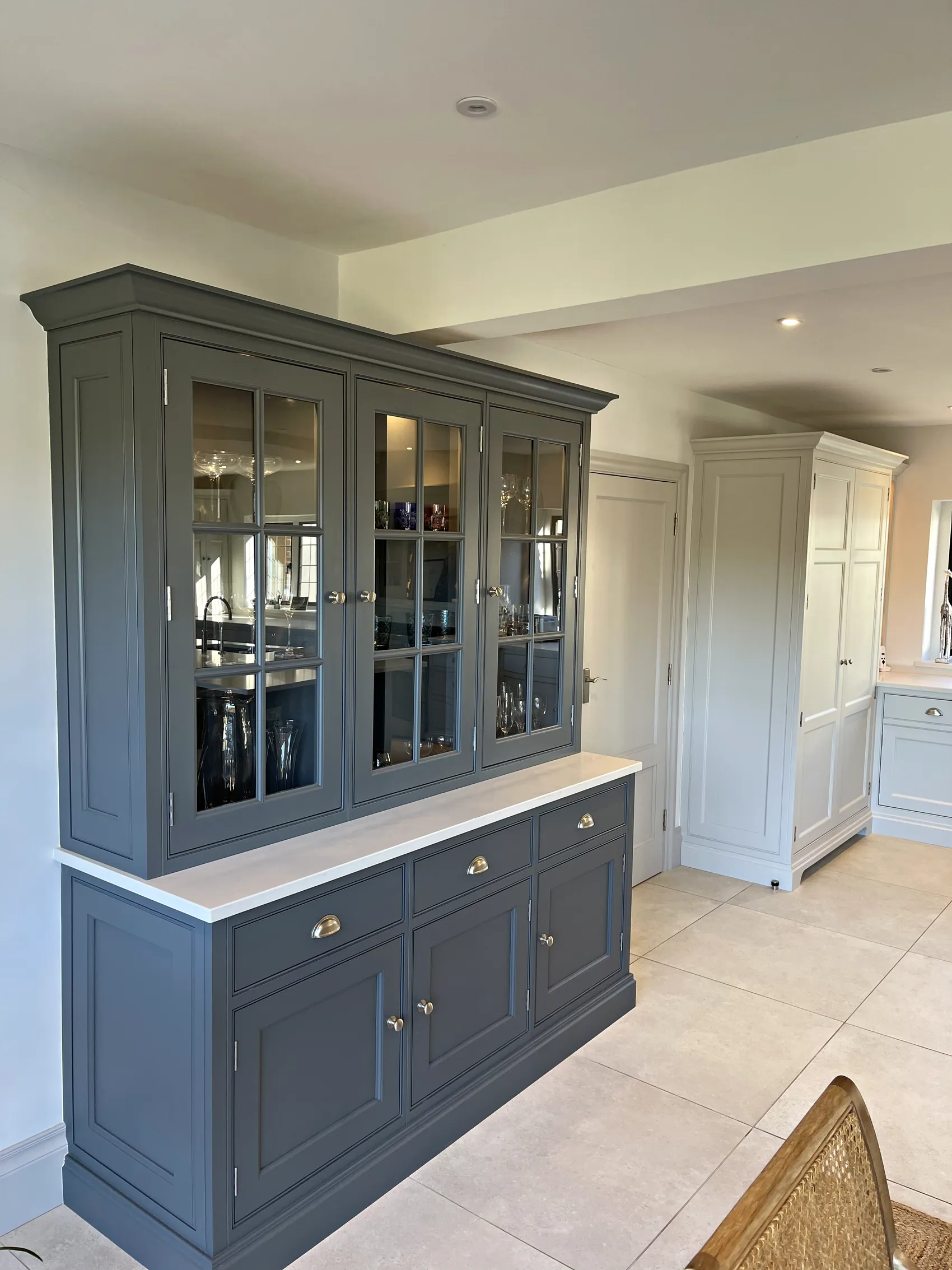 Slate grey glazed dresser with cup handled drawers and a tall pale larder cupboard beyond