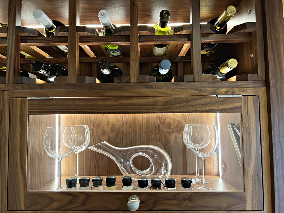 Lit walnut display niche holding a decanter and wine glasses below diamond racks