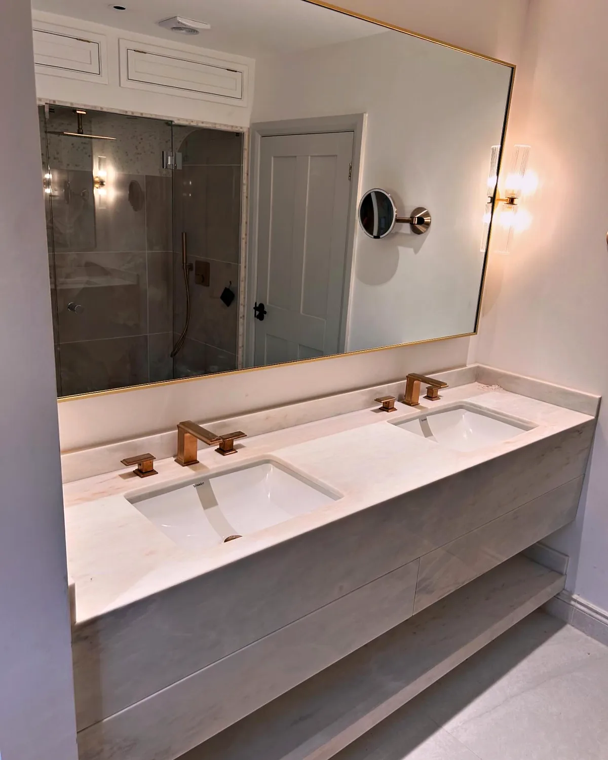 Double basin vanity with a pale marble top, brushed brass taps and a large brass framed mirror