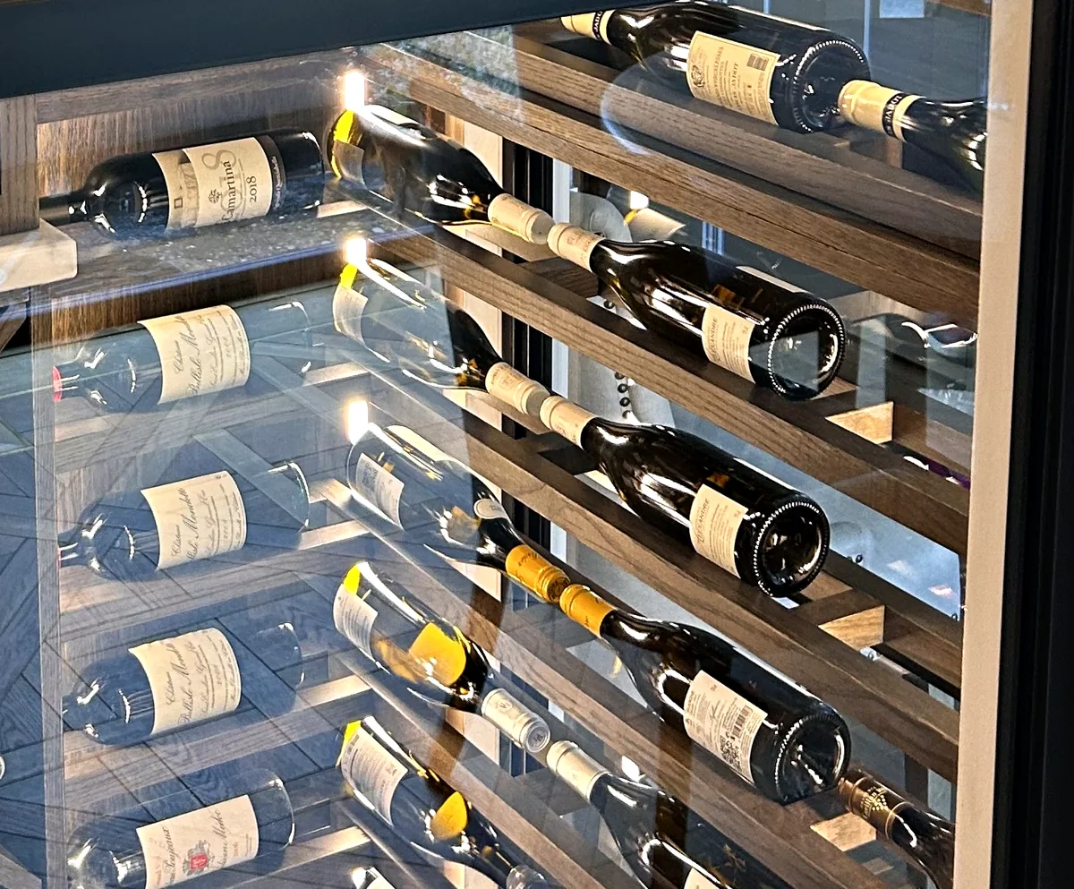 Lit wine wall with bottles resting at an angle on dark wood racks behind glazing