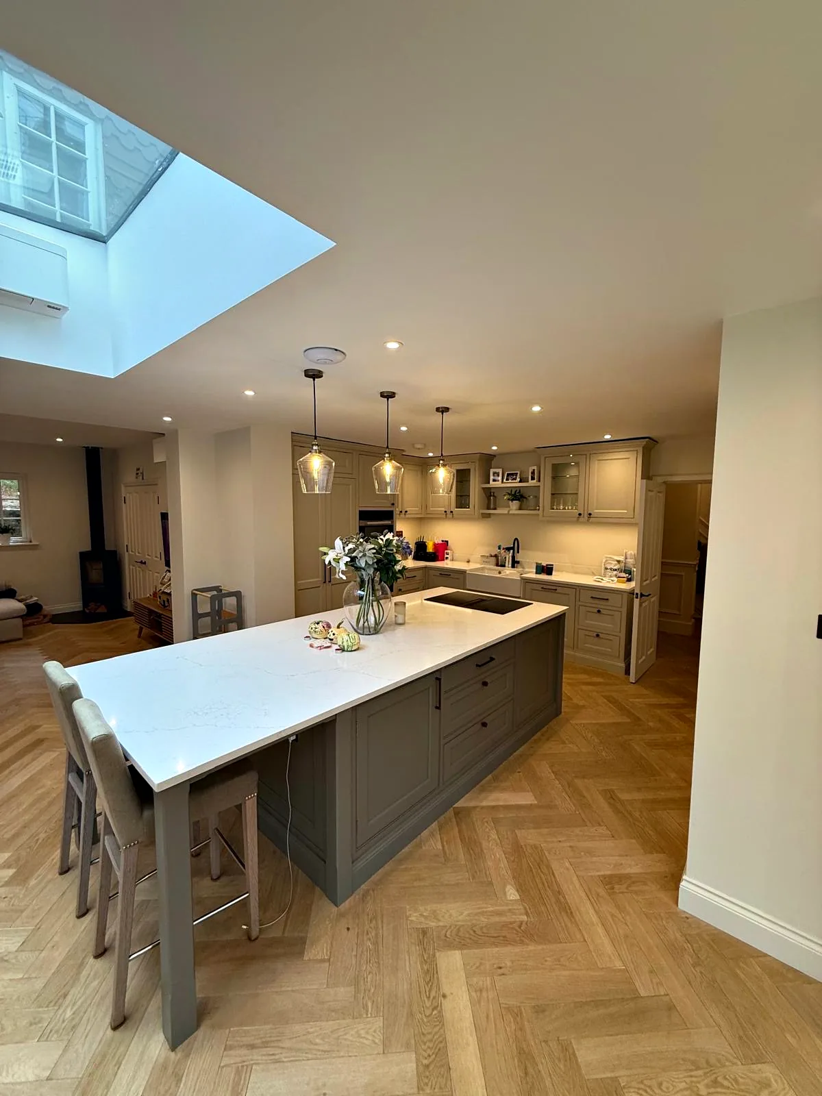 Long kitchen at The Hollowes with a grey island, a white quartz breakfast bar with stools and a roof window above