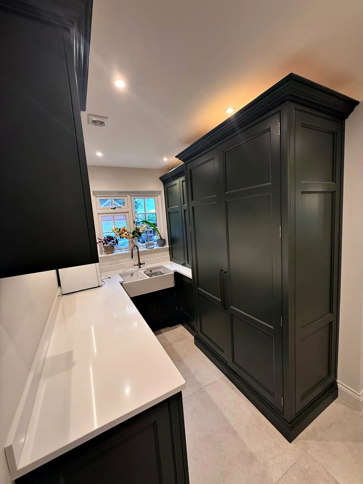 Tall dark green larder cupboard beside a white quartz worktop in a utility room