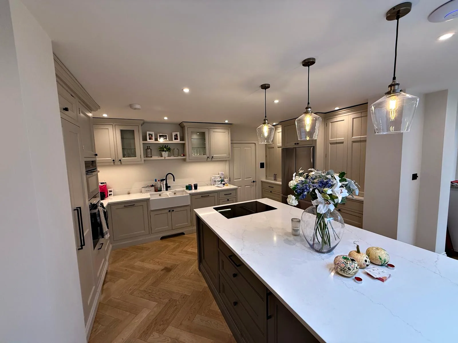 The Hollowes kitchen in pale greige with a dark island, a white quartz top and glass pendants over a herringbone oak floor