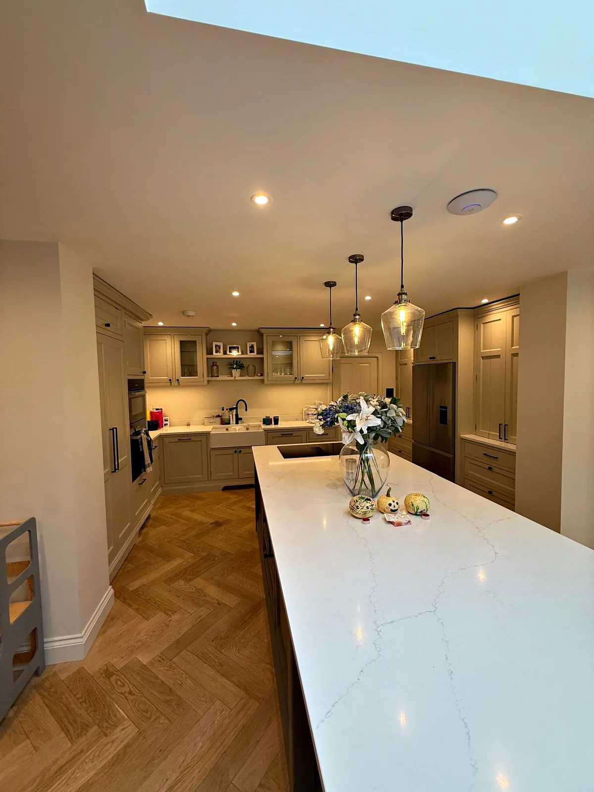 View along the long island with a white quartz top towards the pale greige kitchen