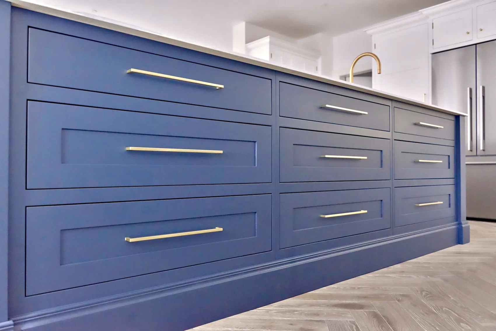 Deep blue island drawers with long brushed brass bar handles on a herringbone floor