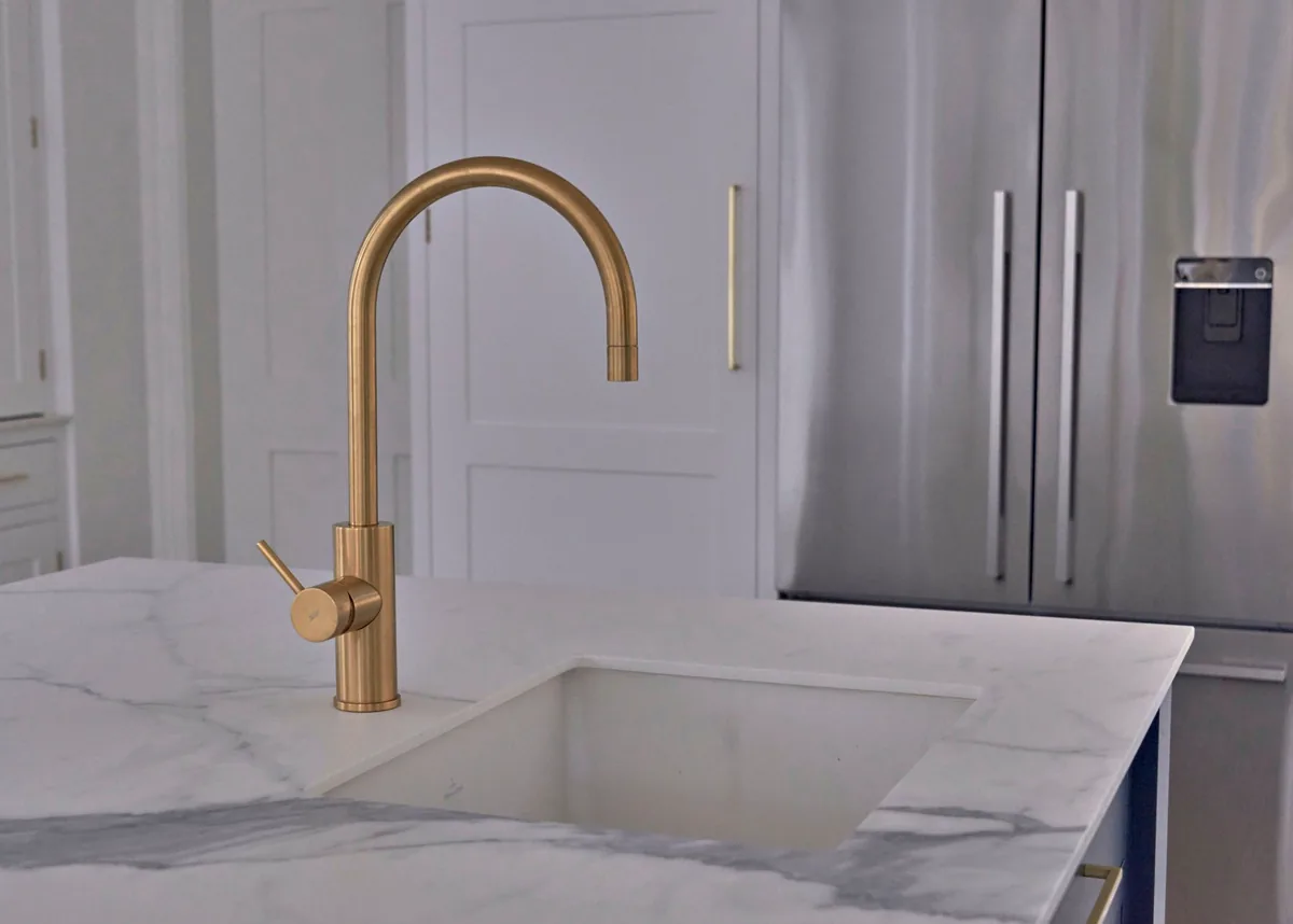 Brass tap over an undermount sink in a marbled quartz worktop