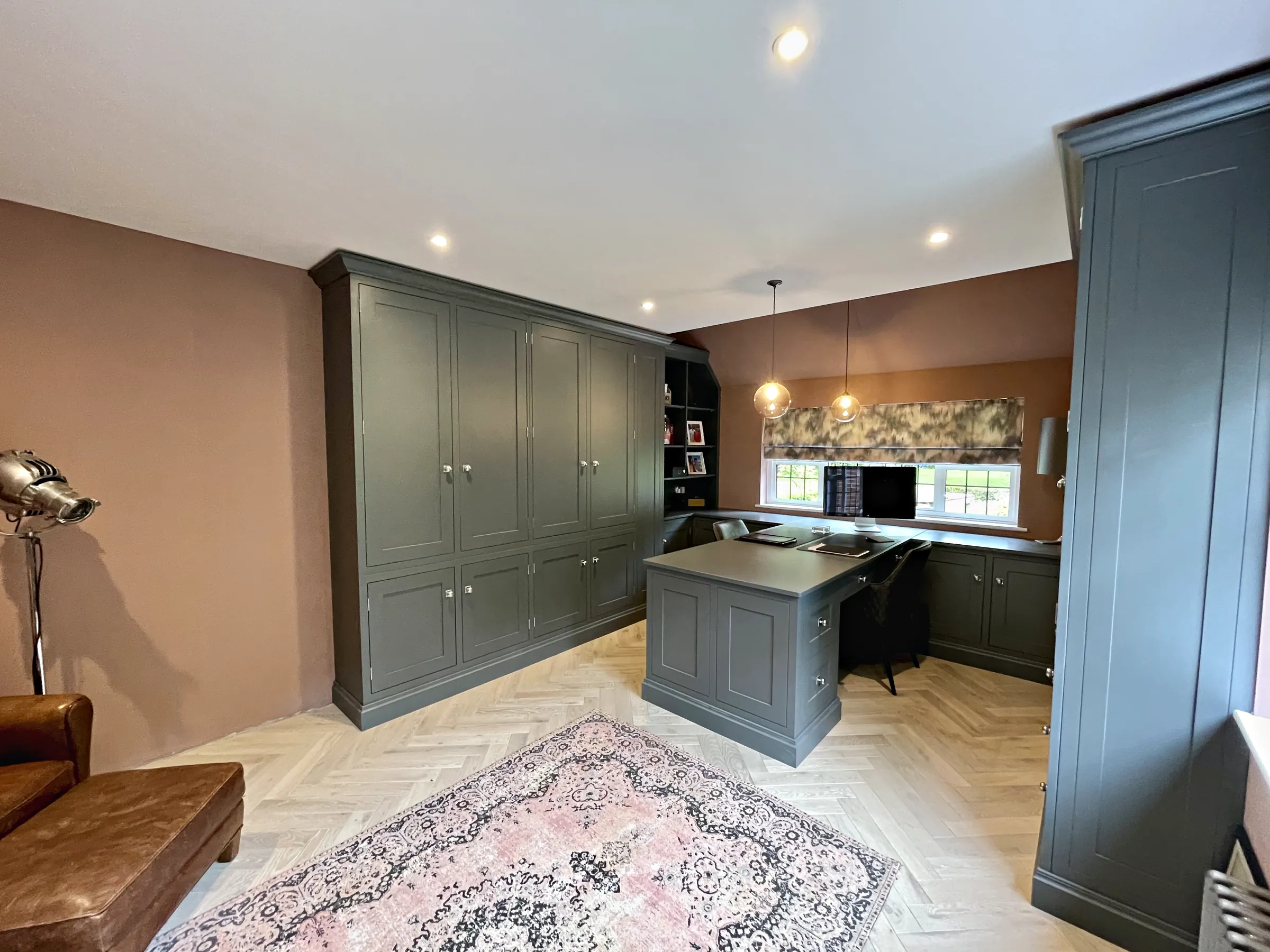 Grey green study cabinetry with a desk peninsula under glass pendants and pink plaster walls