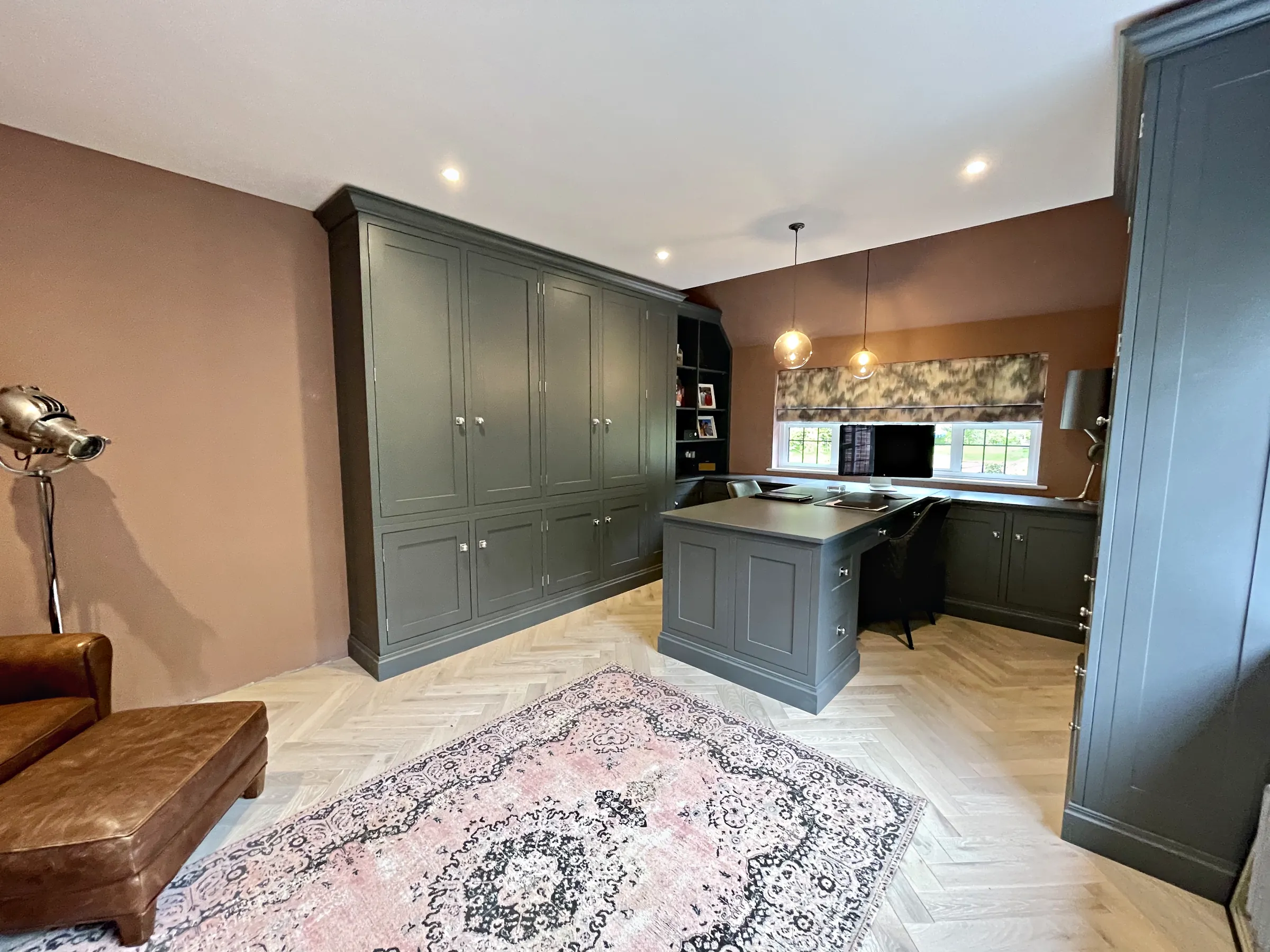 Study with full height grey green cupboards, a desk run and a desk peninsula on herringbone oak