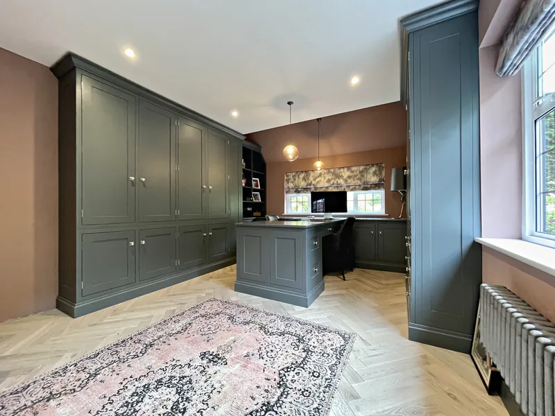 Grey green study cupboards and a desk run under the window with pink plaster walls