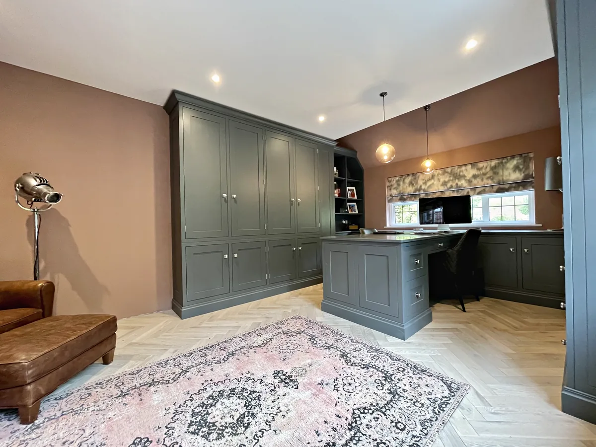 Munstead Plat study with a wall of grey green cupboards and a desk peninsula under glass pendants