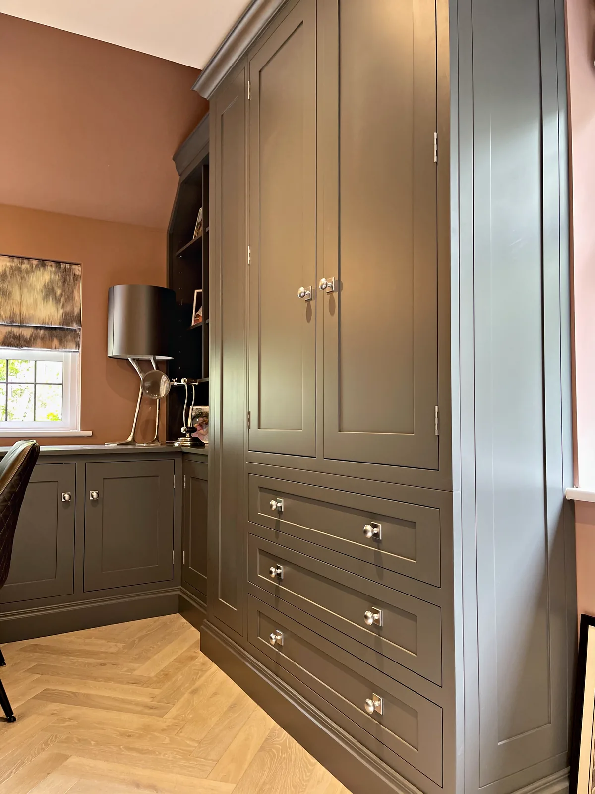 Tall grey green cupboard over a bank of drawers with nickel knobs in a study