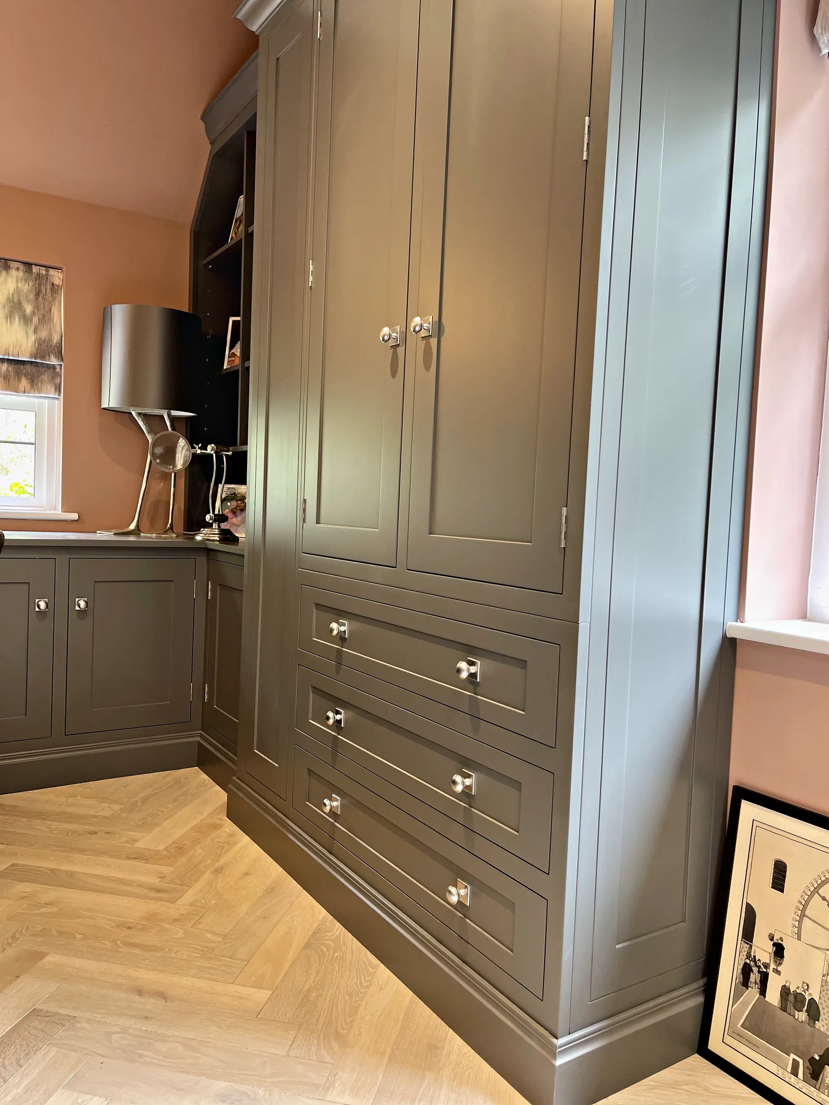 Tall grey green cupboard over a bank of drawers with nickel knobs on a herringbone floor