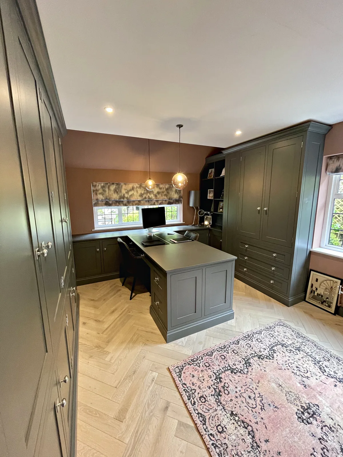 Study with full height grey green cupboards, a desk peninsula with drawers and a desk run under the window