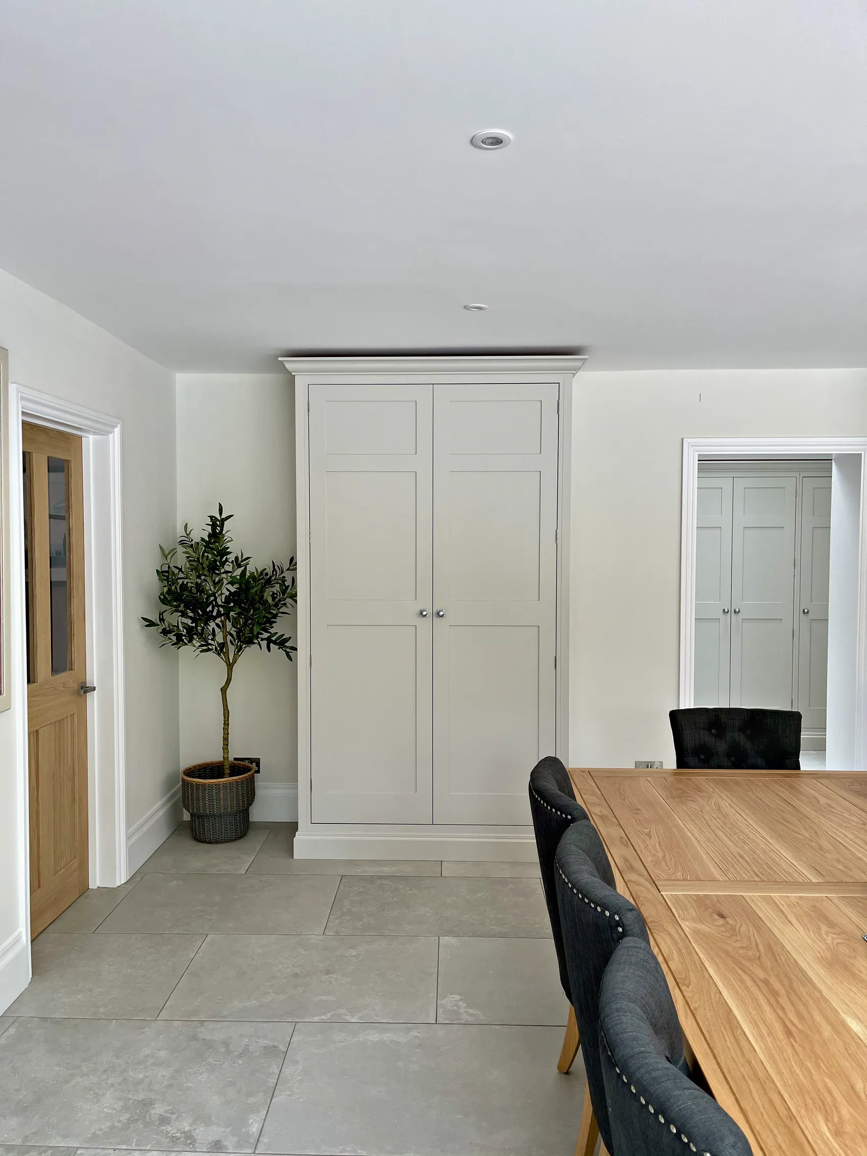 Freestanding pale grey larder cupboard with a cornice between an oak door and a doorway