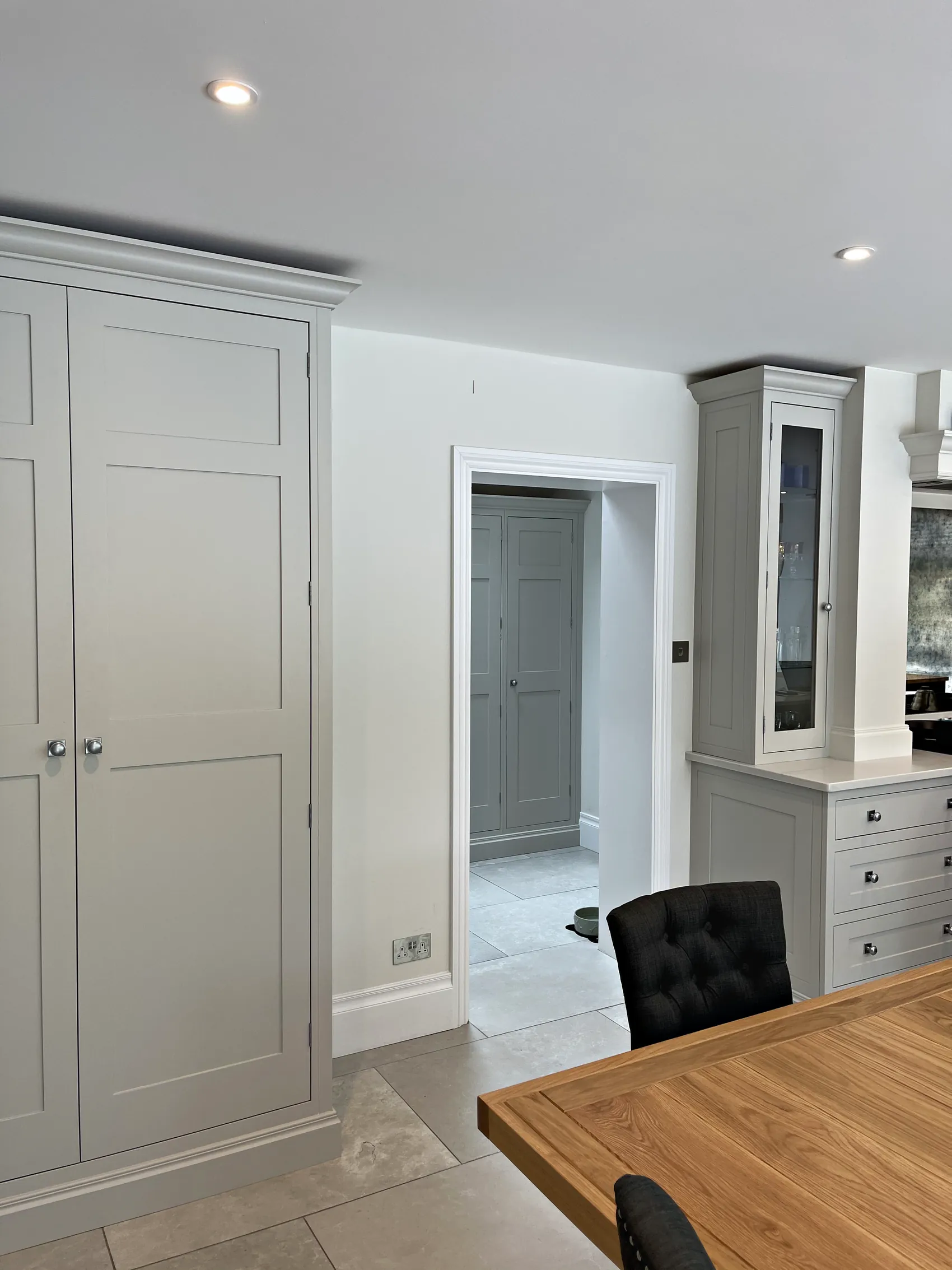 Tall pale grey freestanding larder cupboard beside a glazed dresser at the end of a kitchen