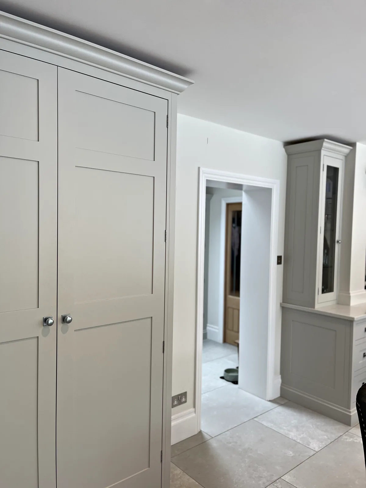 Tall pale grey panelled cupboard doors with nickel knobs beside an open doorway