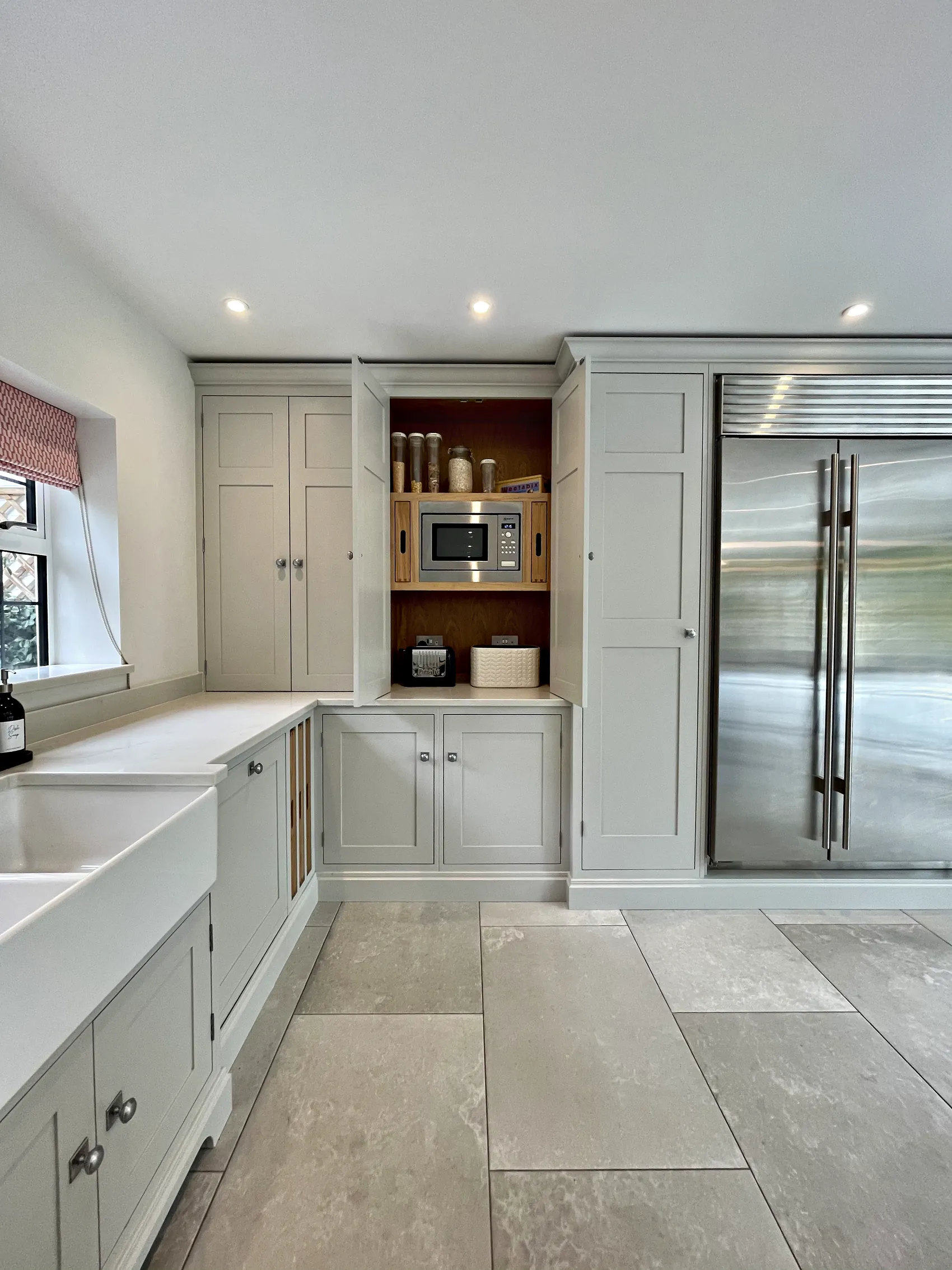 Pale grey kitchen run with a twin Belfast sink, an oak lined breakfast larder and a steel fridge freezer