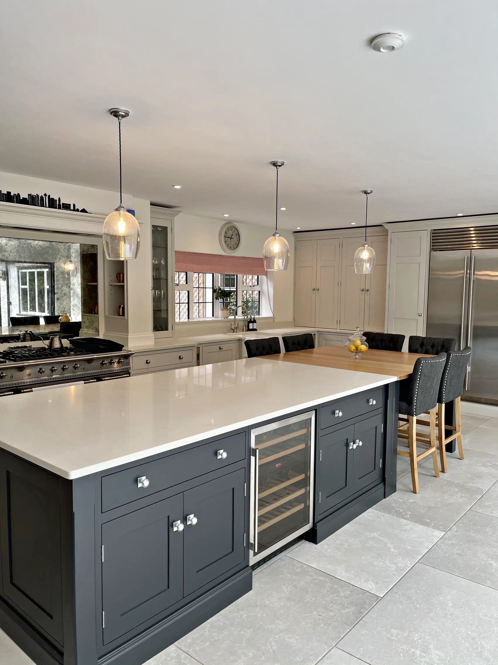 Charcoal navy island with a white quartz top, wine cooler and nickel knobs before a pale grey range wall